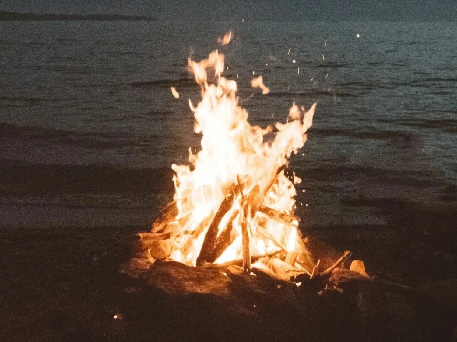 A large bonfire on a beach at night with waves in the background.