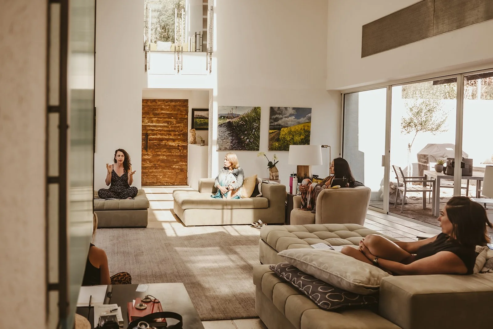 People having a discussion in a bright, spacious living room with large windows and outdoor patio.