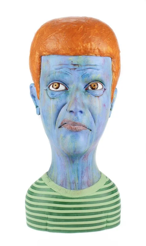 A bust of a humanoid figure with blue skin, red hair, and yellow eyes, wearing a green and white striped shirt.