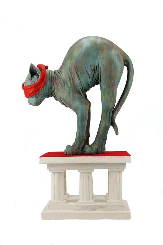 A sculpture of a creature with the body of a dog or cat and the head of an elephant, wearing a red scarf and standing on a pedestal.