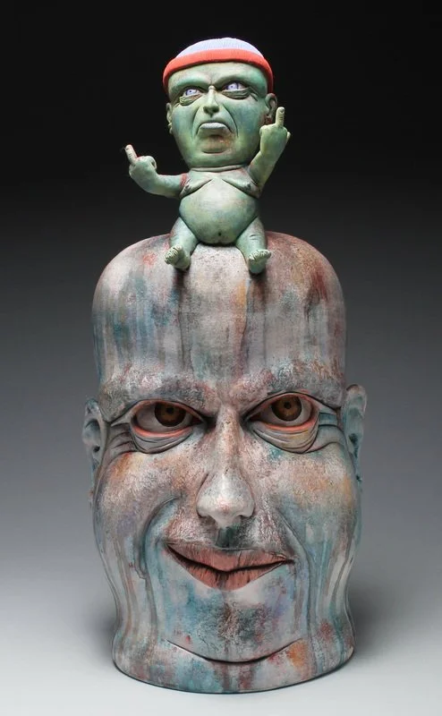 A sculpture of a large human head with a smaller cartoonish character sitting on top, both with unusual features and exaggerated expressions.