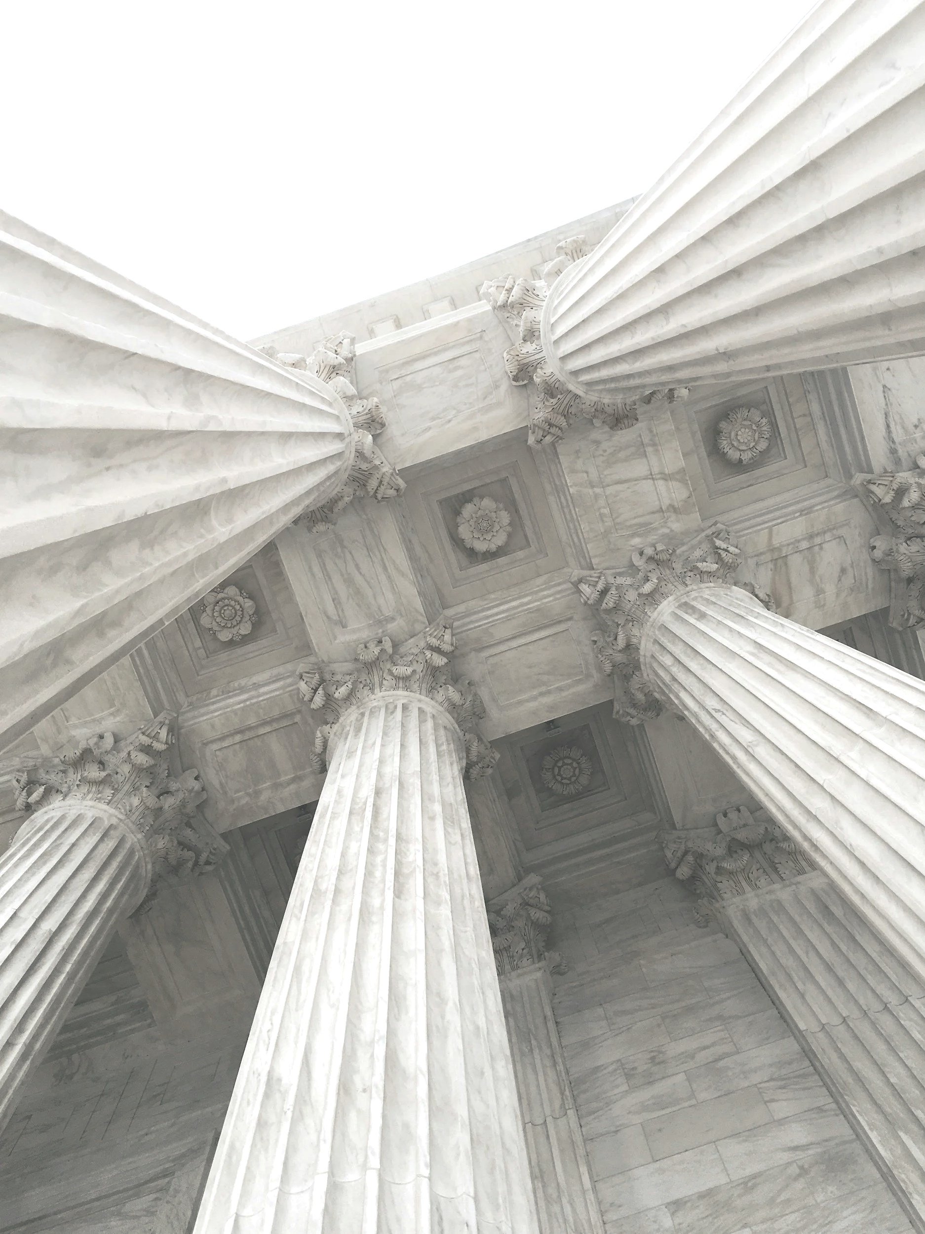 Looking up at tall marble Corinthian columns inside a classical building with decorative ceiling panels.