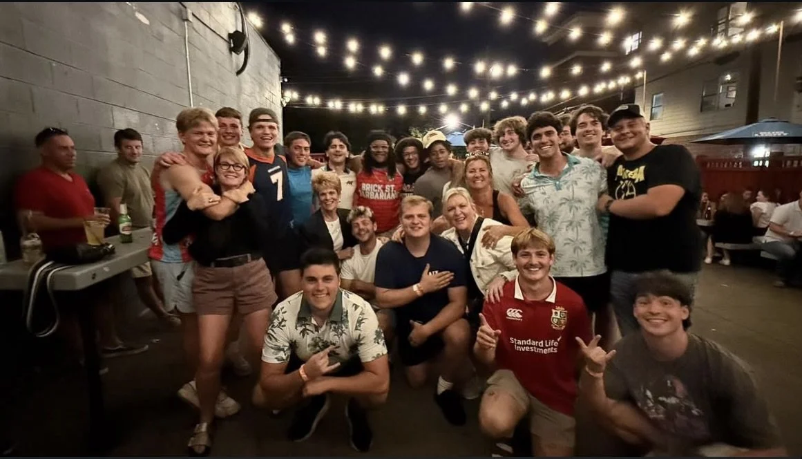 A large group of young people gathered at an outdoor event, smiling for the camera under string lights at night.