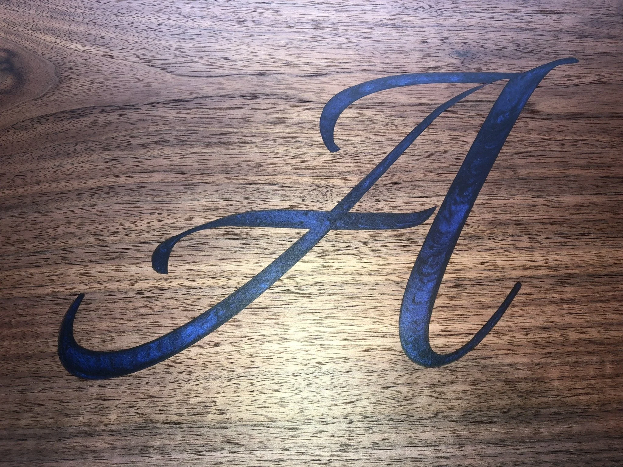 A metal monogram of the letter 'J' with a script-style font, placed on a wooden surface.
