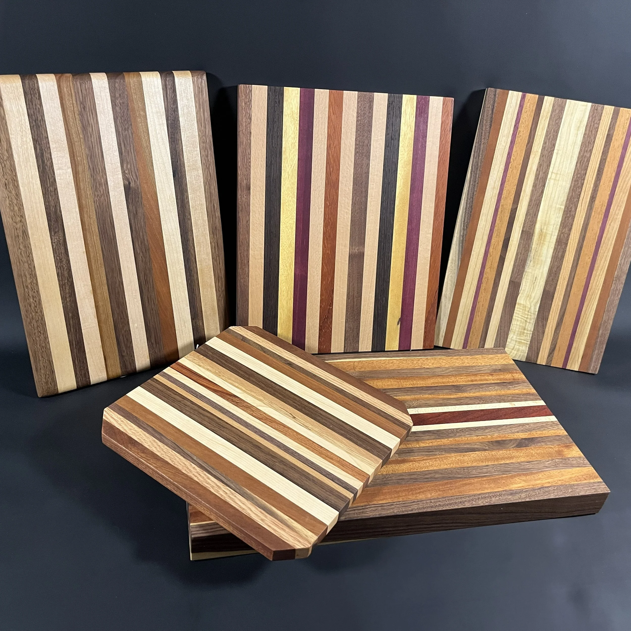 Multiple wooden cutting boards with colorful striped patterns on a dark surface.