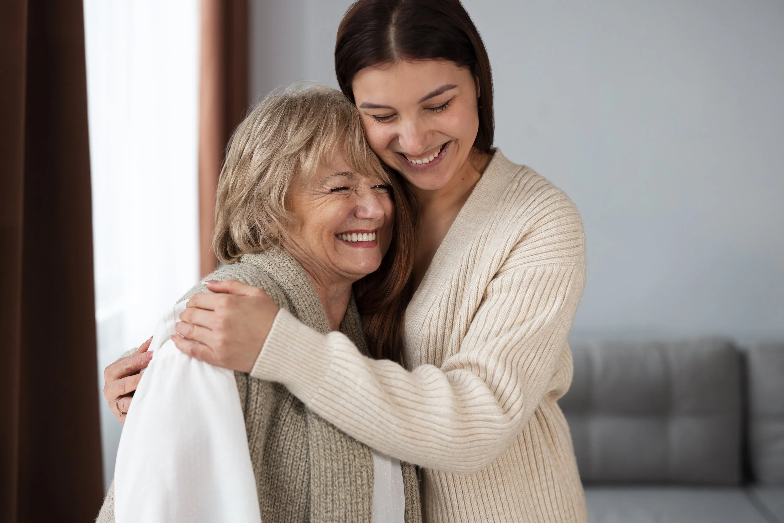 A young woman and an elderly woman hugging and smiling happily indoors.