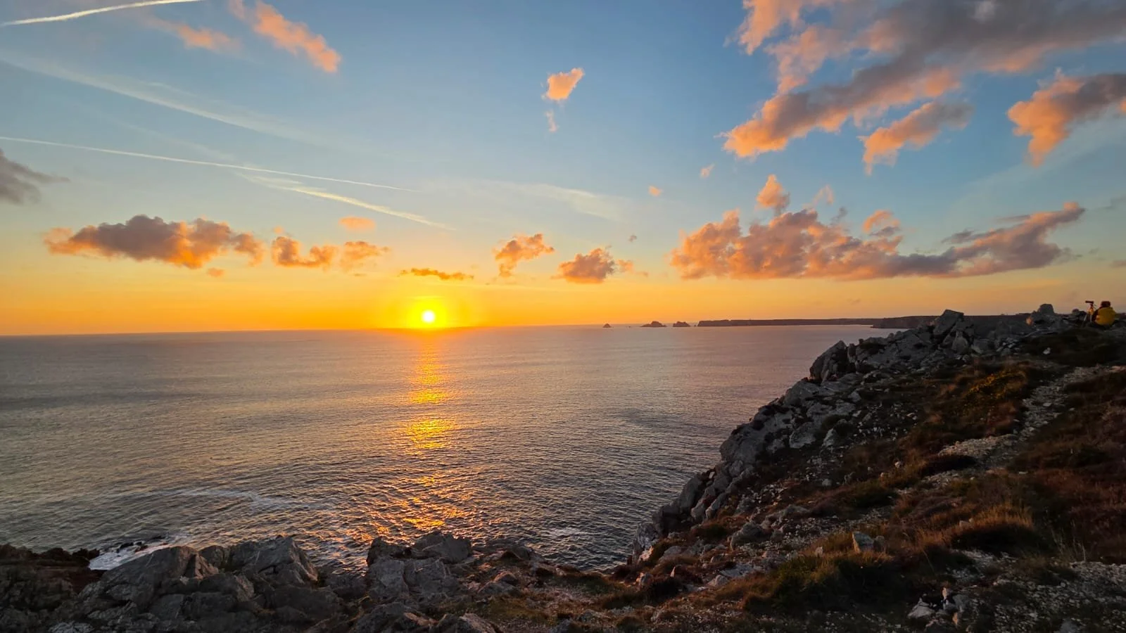 Coucher de soleil sur la mer vu depuis une falaise rocheuse avec des nuages orange dans le ciel