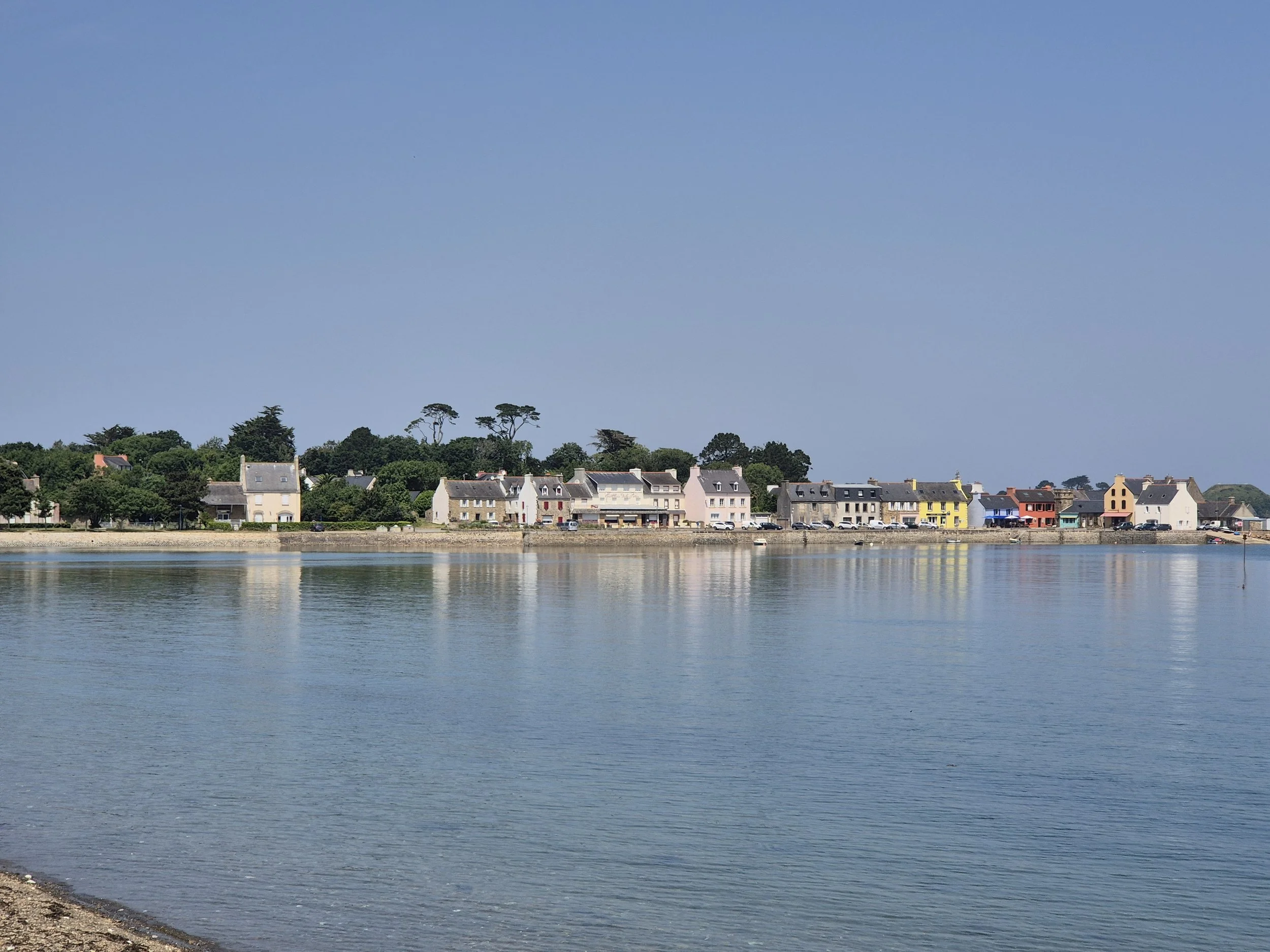 Un village côtier avec des maisons colorées au bord de l'eau, sous un ciel bleu clair.