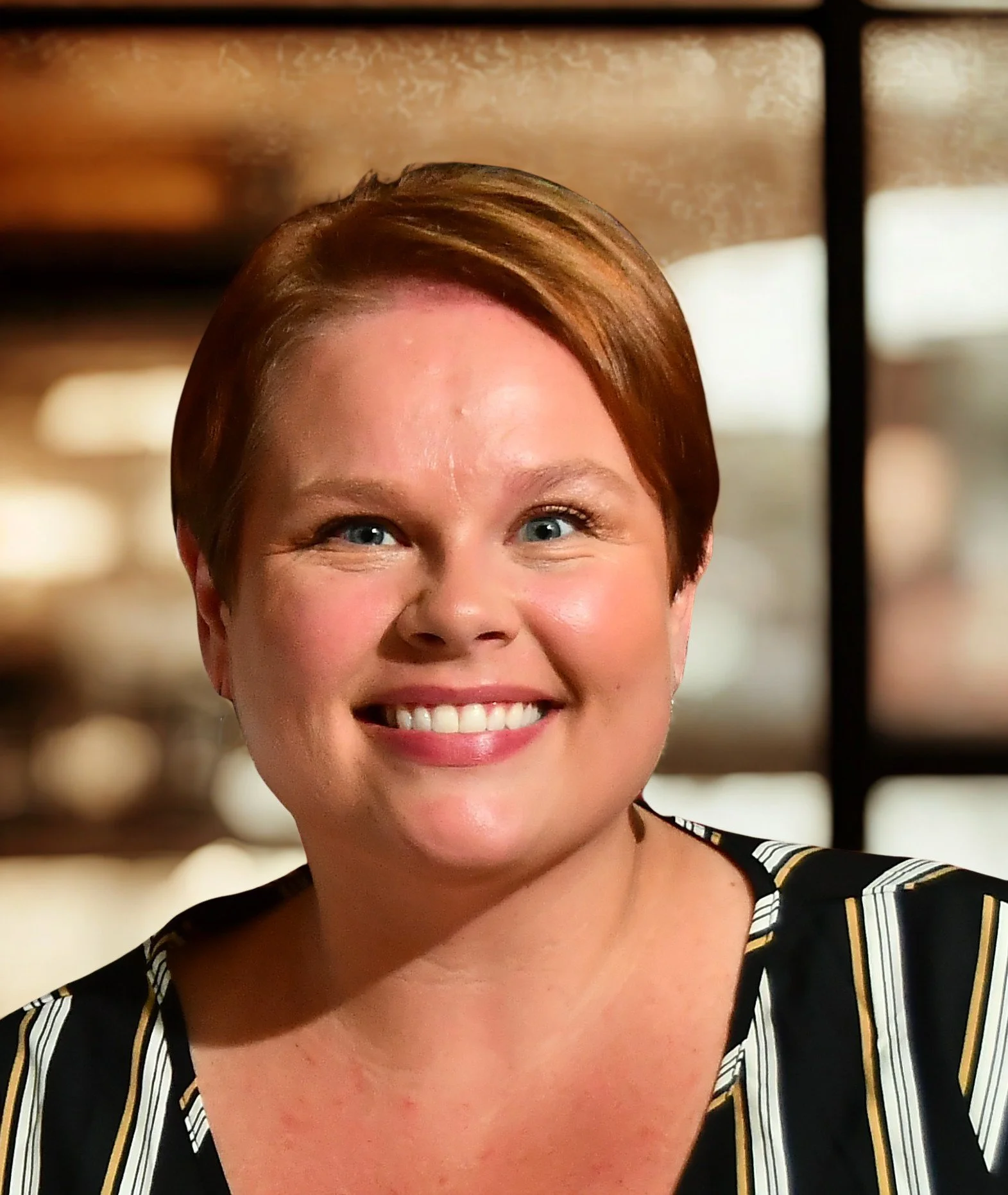 Close-up of Stephanie Ellis a smiling woman with short red hair, blue eyes, wearing a black and white striped top.