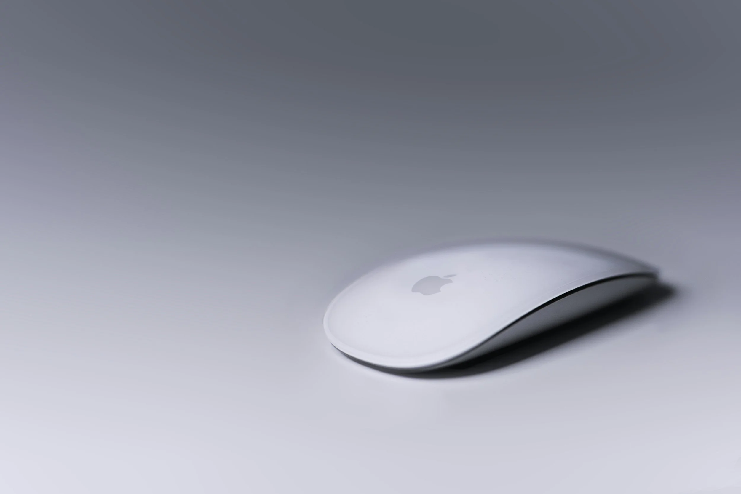 A white Apple Magic Mouse resting on a smooth surface with a blurred background.