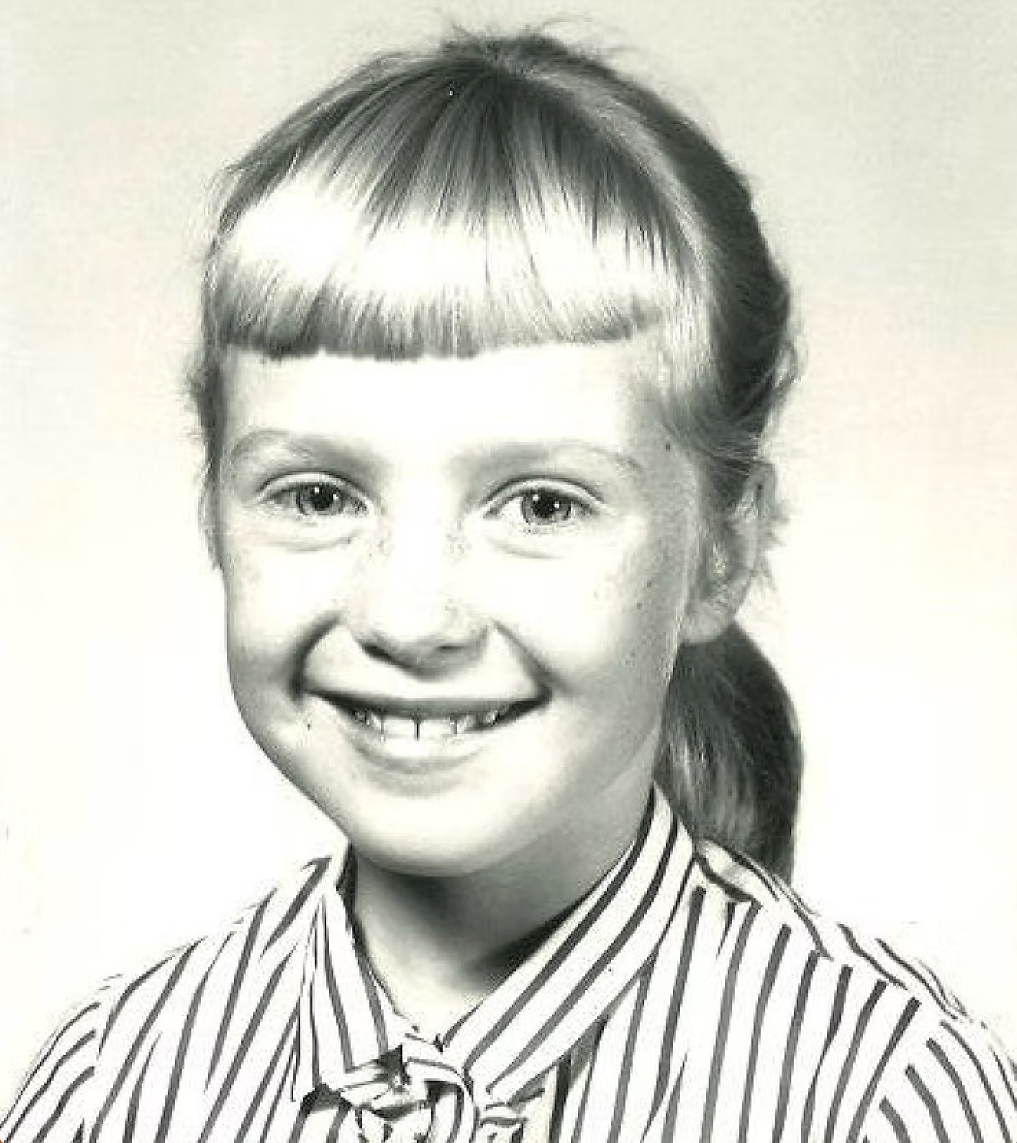 Black and white photo of a young girl with pigtails, wearing a striped shirt, smiling.