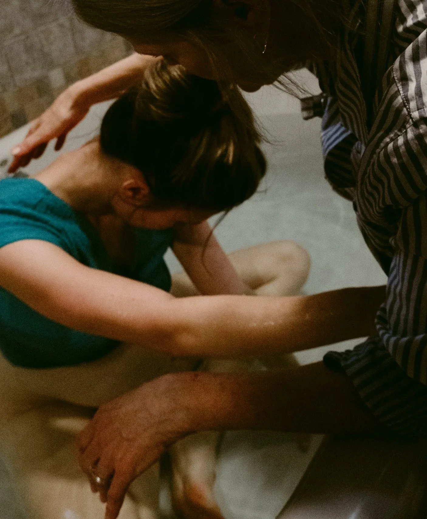 Two women and an elderly man in a bathroom, with one woman holding the man and the other supporting him, perhaps providing assistance or comfort.
