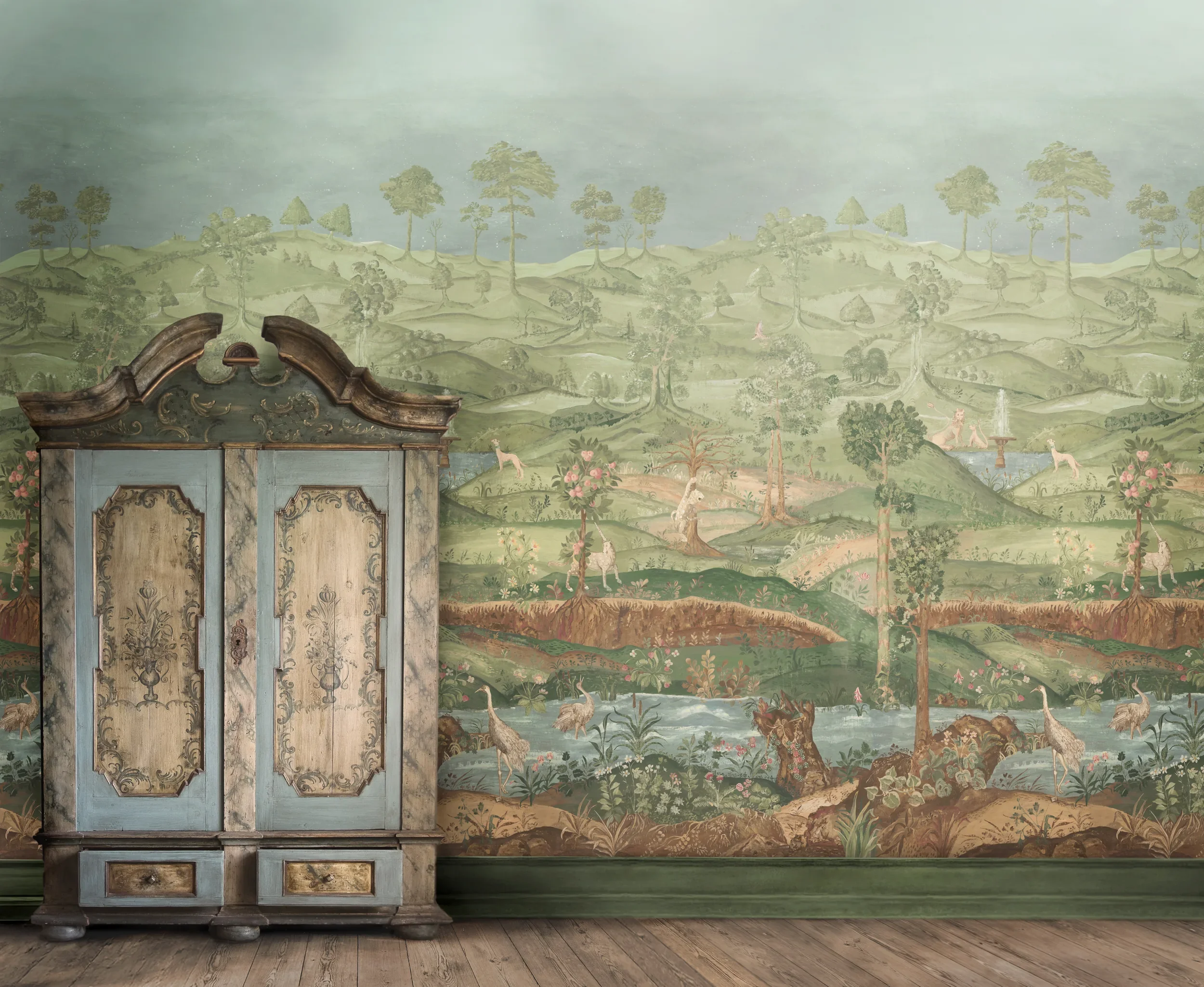 A vintage wooden cabinet in front of a scenic wall painting of a lush green landscape with trees, hills, and animals such as deer and birds.