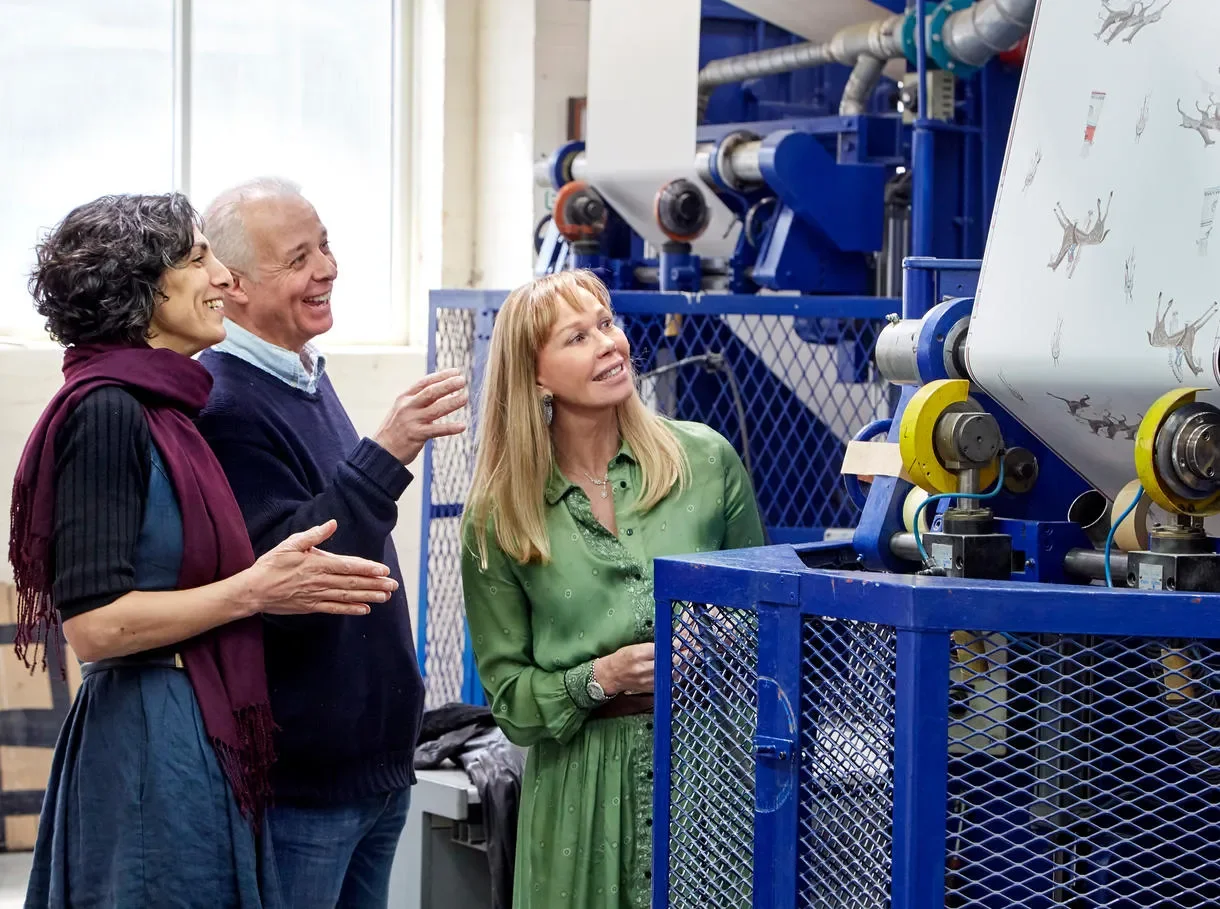 Melissa White and Kit Kemp are photographed smiling as their Friendly Folk wallpaper is printed in a factory.