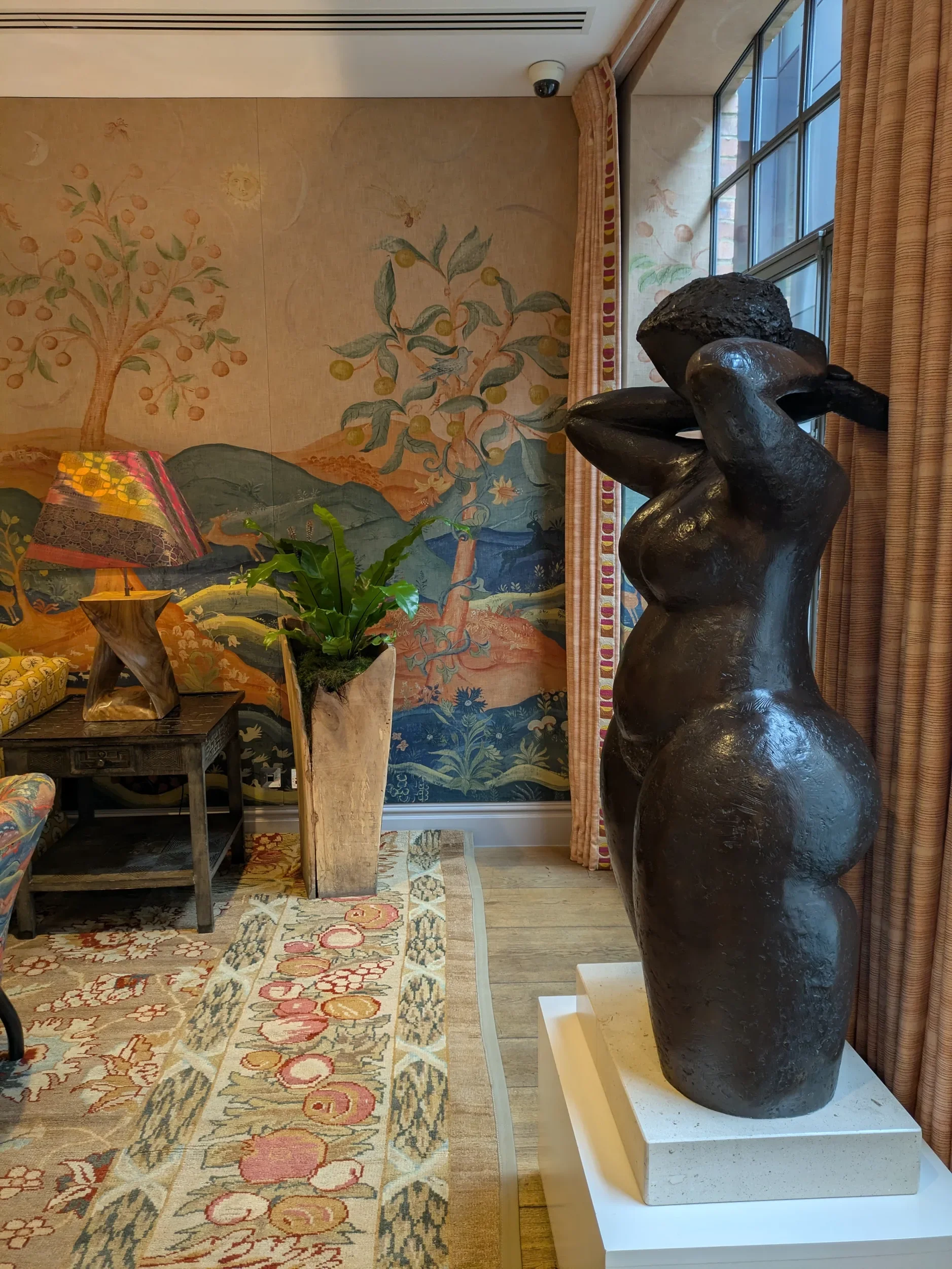 Rufus: Harvest Moon wallpaper by Melissa White for Andrew Martin, shown in a styled interior with a sculptural nude torso, draped curtains, decorative lamp, and patterned rug.