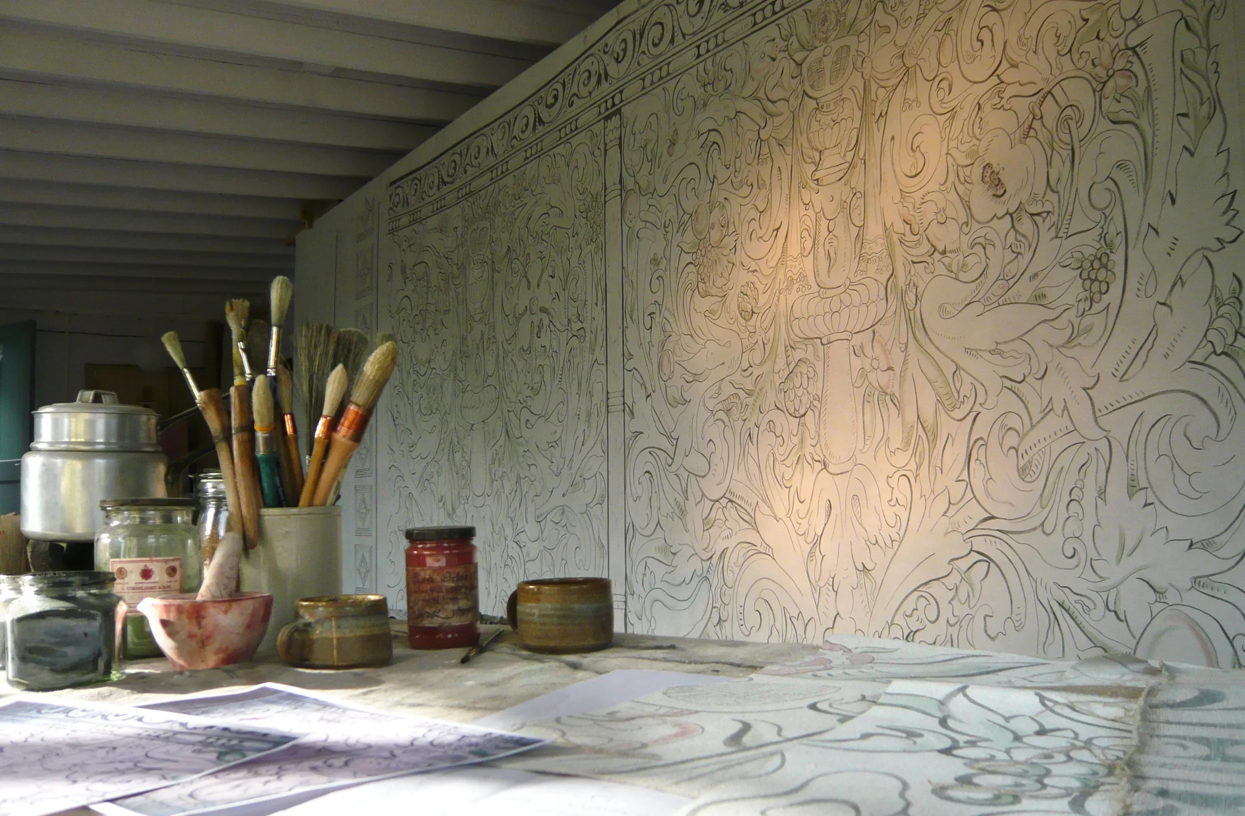 Photo of paintbrushes and paint in front of Melissa White's largescale multivine painted cloths for Stiffkey Old Hall, Norfolk.