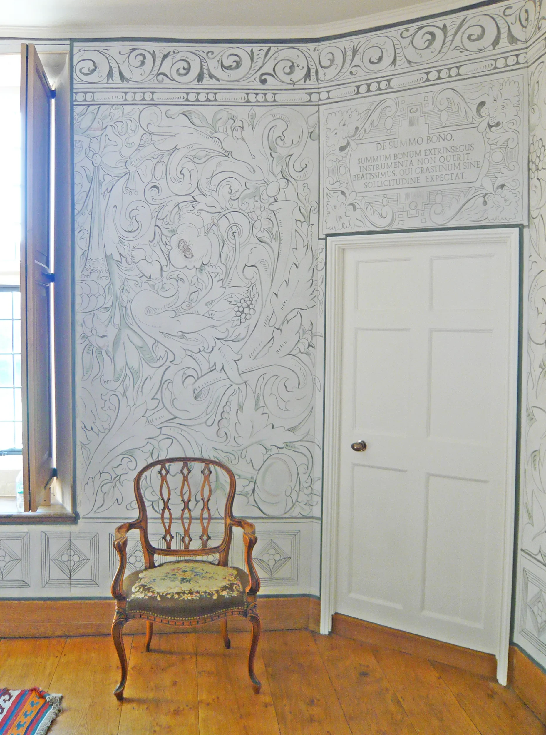 A vintage wooden chair with a floral seat cushion in front of Melissa White's largescale multivine painted cloths for Stiffkey Old Hall, Norfolk.