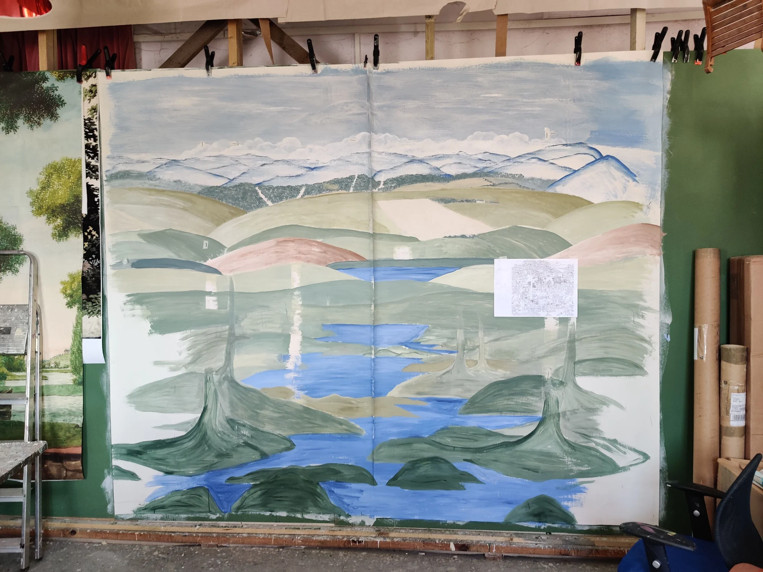 A painted landscape mural showing mountain ranges, rolling hills, a river, and sky with clouds.