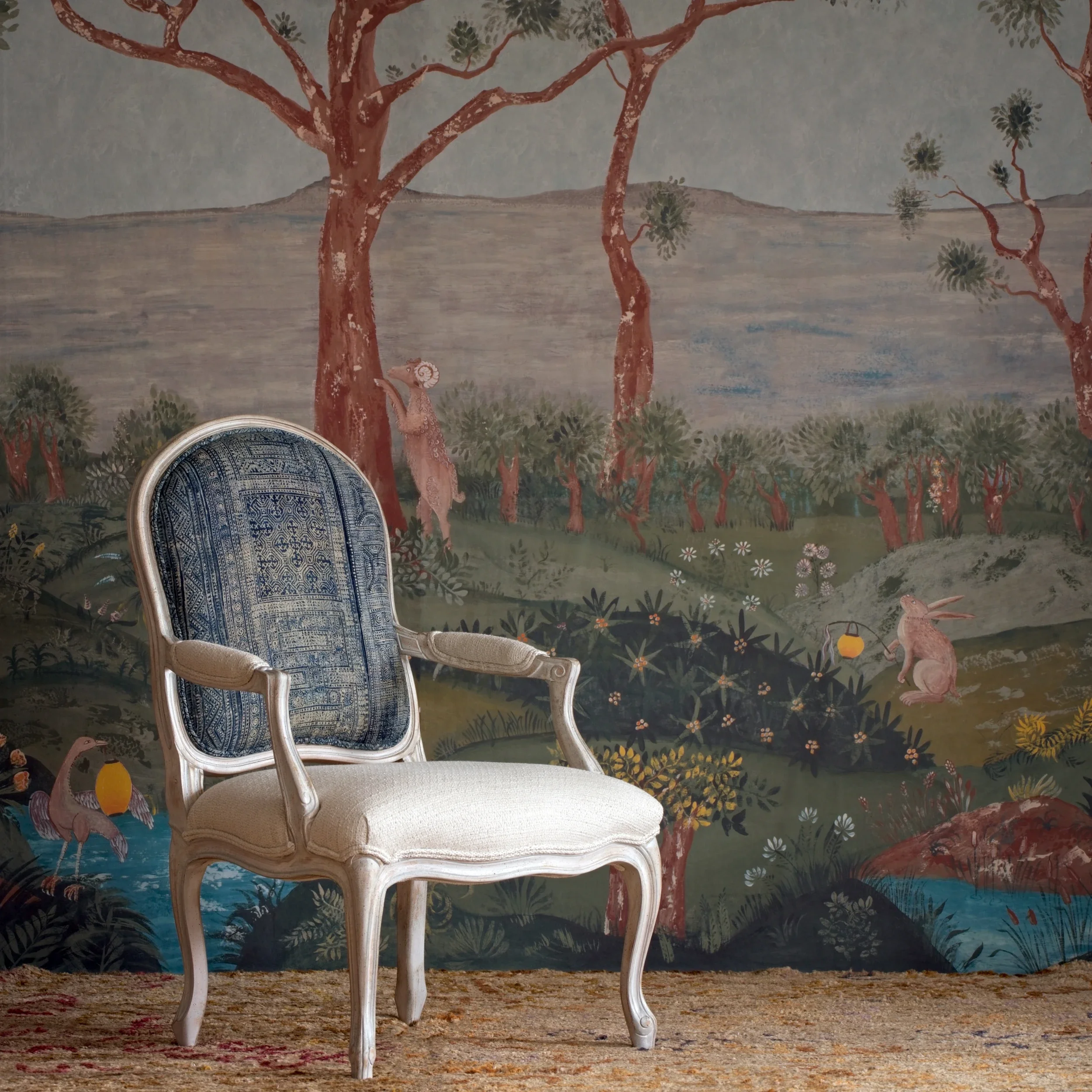 Elegant antique chair with blue patterned upholstery in front of a scenic mural depicting trees, mountains, and animals.