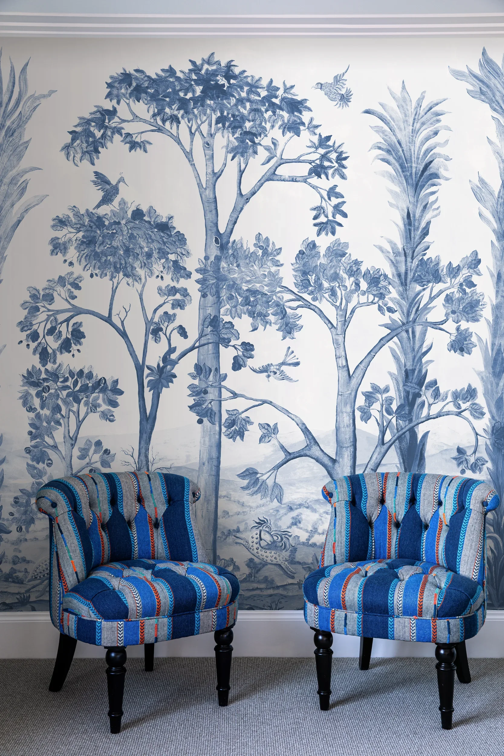Tall Trees wallpaper by Melissa White for GP&J Baker, Kit Kemp Wallpaper collection, in the Delft Blue colourway. Two upholstered chairs stand in front of the wallpaper.