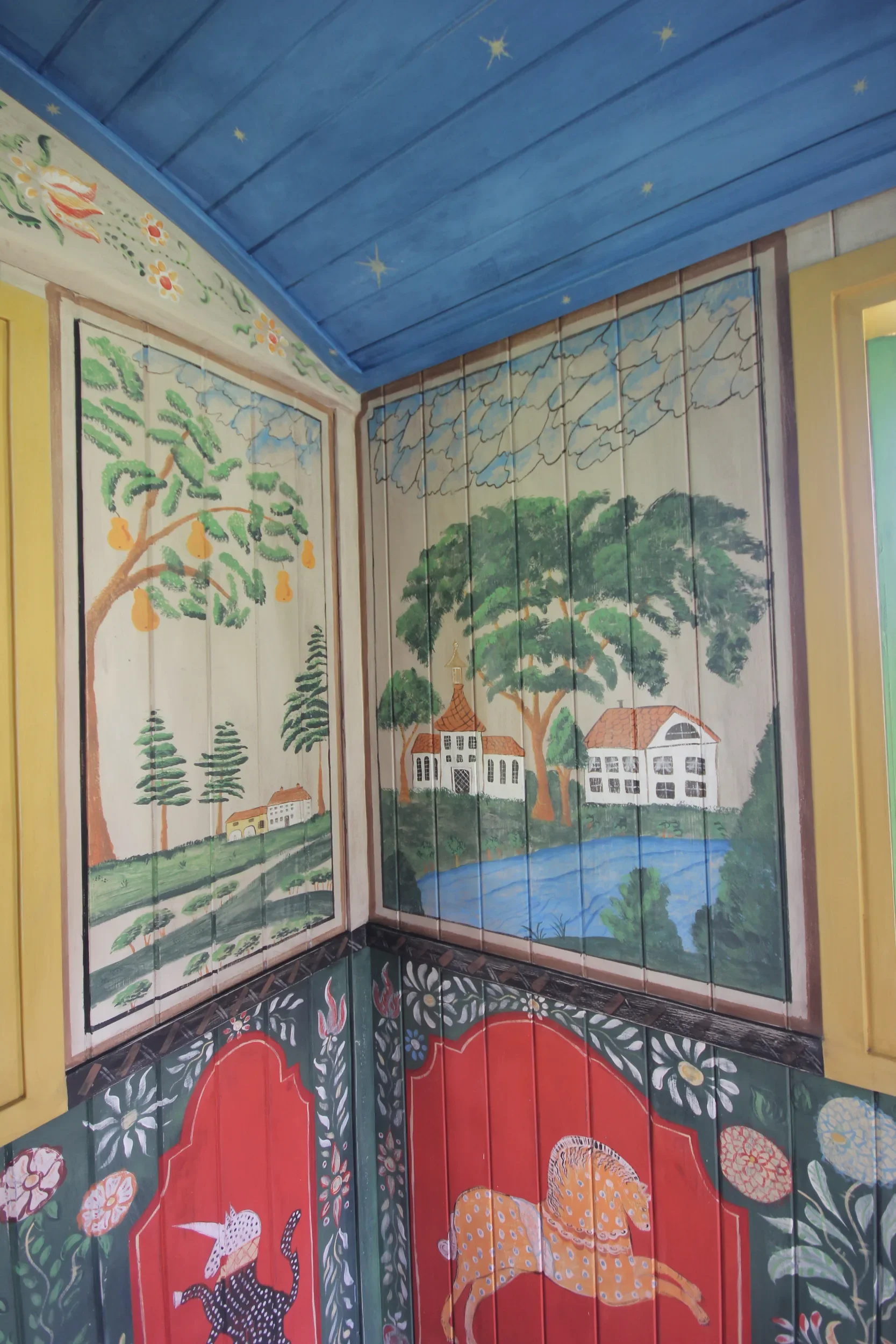The corner interior of Kit Kemp's Shepherd's Hut, New Forest, painted by Melissa White, 2019. Folk art panels with a blue starry ceiling.
