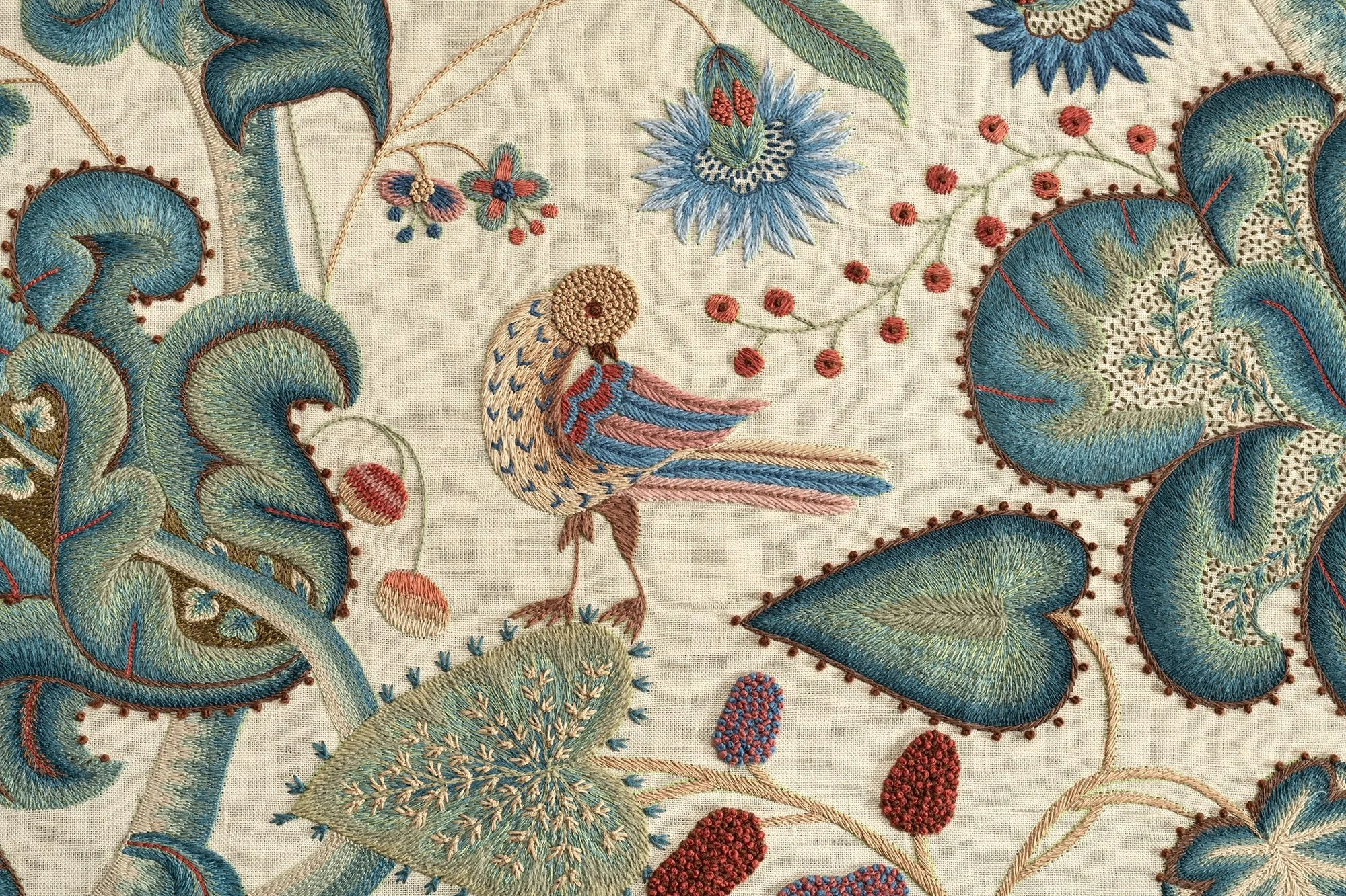 Embroidery of a bird surrounded by blue and red floral patterns on a beige fabric background.