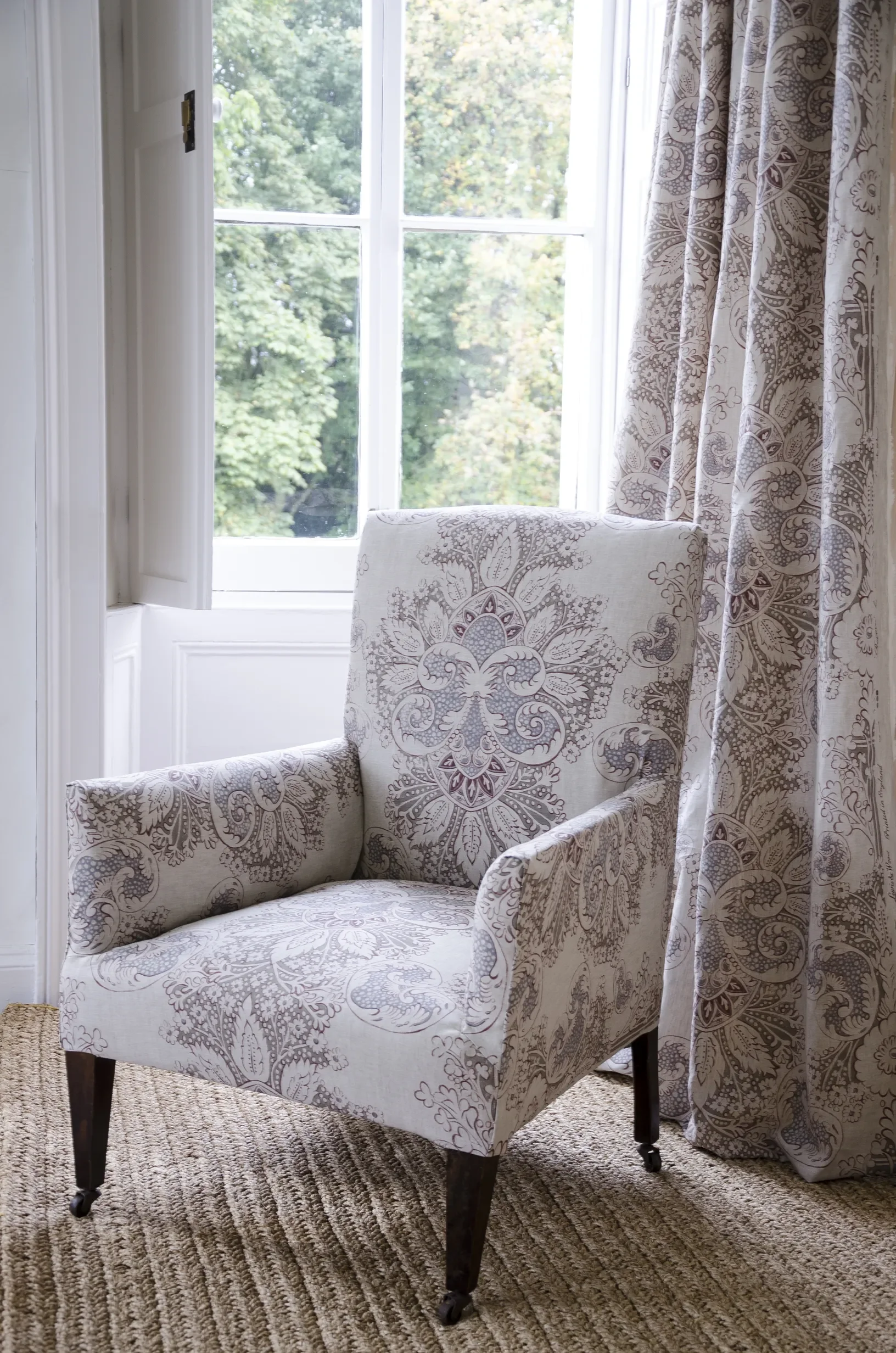 Chair upholstered in Rococo fabric by Melissa White for Lewis & Wood, shown alongside matching curtains, displaying the hand-painted ornamental repeat design.