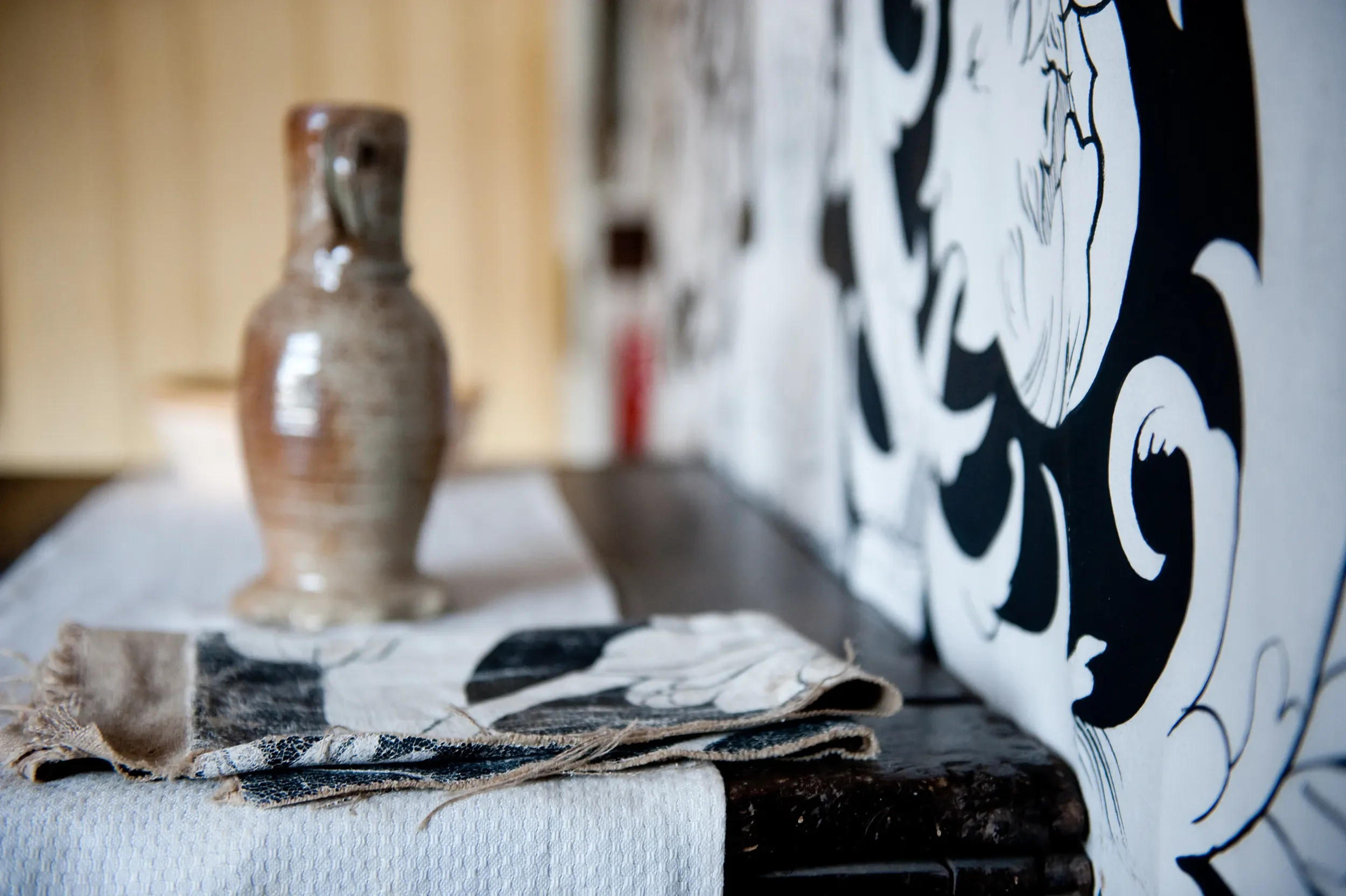 Close-up of a ceramic vase on a table against the backdrop of painted cloths by Melissa White at Shakespeare's Birthplace Museum.