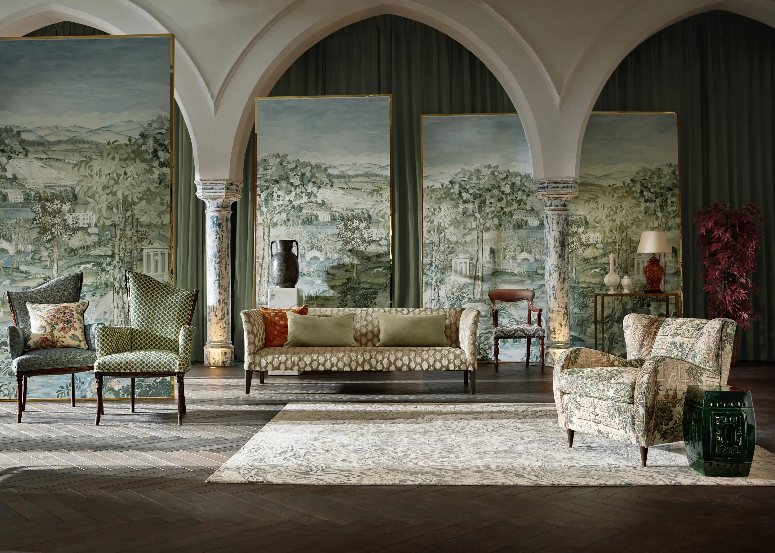 Interior of a room with arched ceilings, painted mural of a landscape on the wall, various upholstered chairs, a sofa, and decorative vases and lamps.