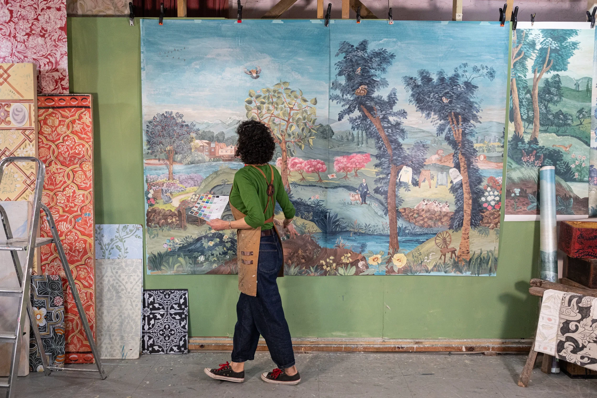 Melissa White is dwarfed in front of her large-scale painting for the John Smedley 240th anniversary collaboration. She is wearing jeans and an apron at her Hastings studio.