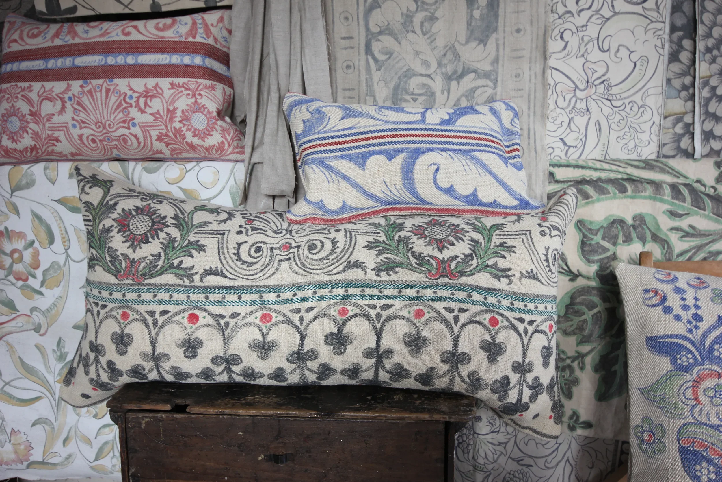 Hand-painted cushions by Melissa White for Le Bon Marché, Paris, showing a selection of designs drawn from historic sources, arranged on a wooden surface.