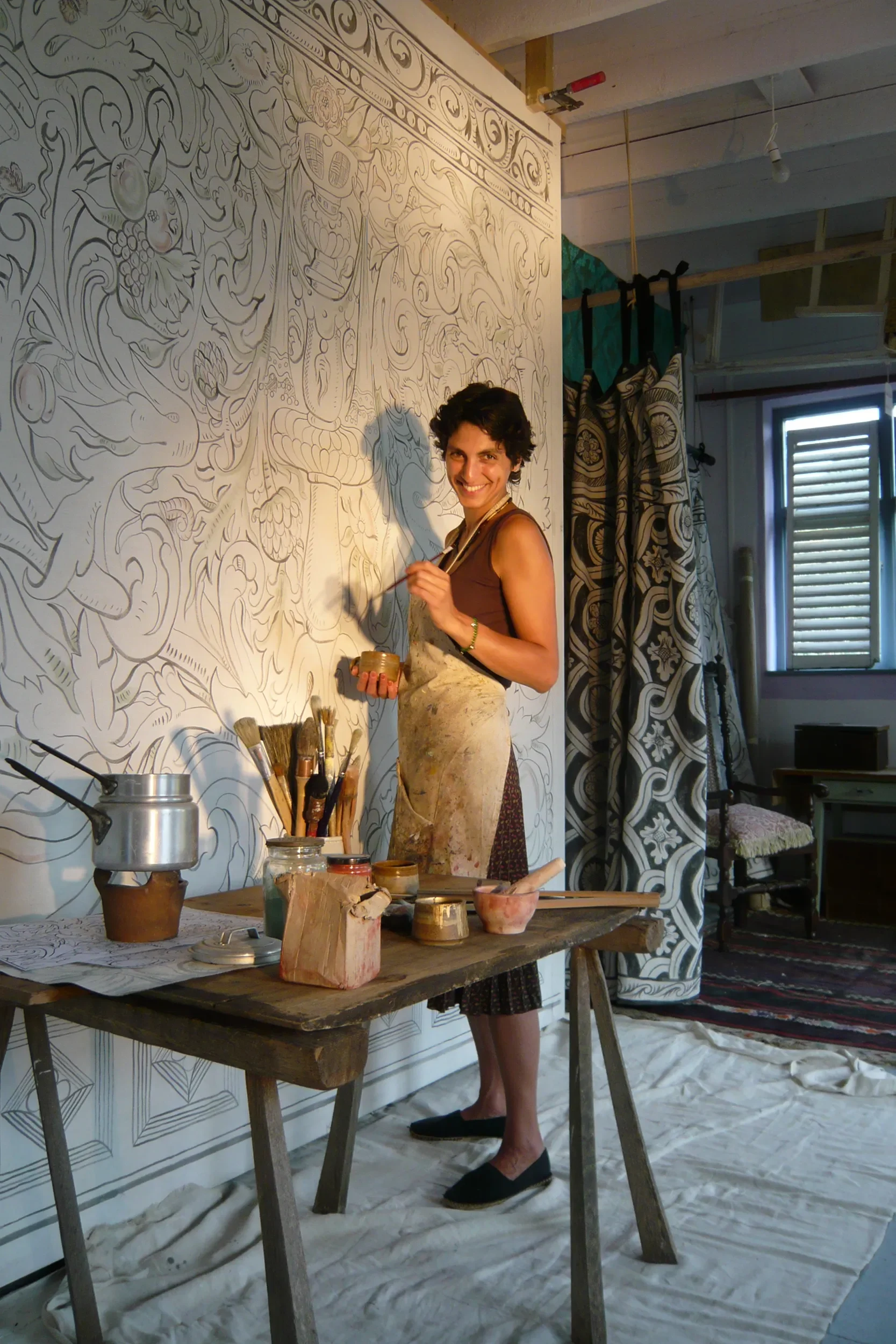 Melissa White standing painting in front of her largescale multivine painted cloths for Stiffkey Old Hall, Norfolk. Pictured in Melissa's Hastings studio.