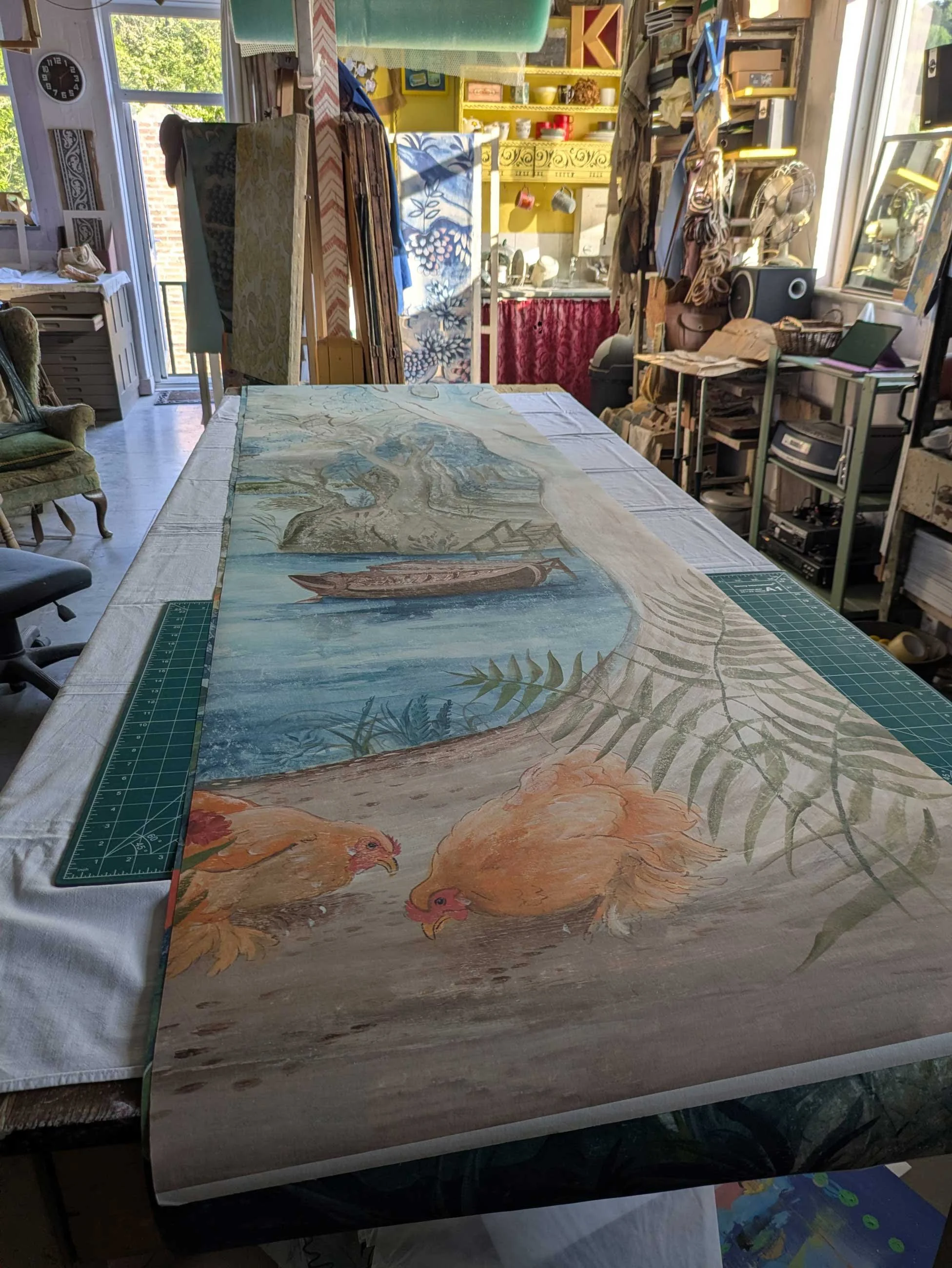 A long-scale wallpaper panel of Glimpses of Thyme unrolled on a studio table, featuring the Cochin hen motif.
