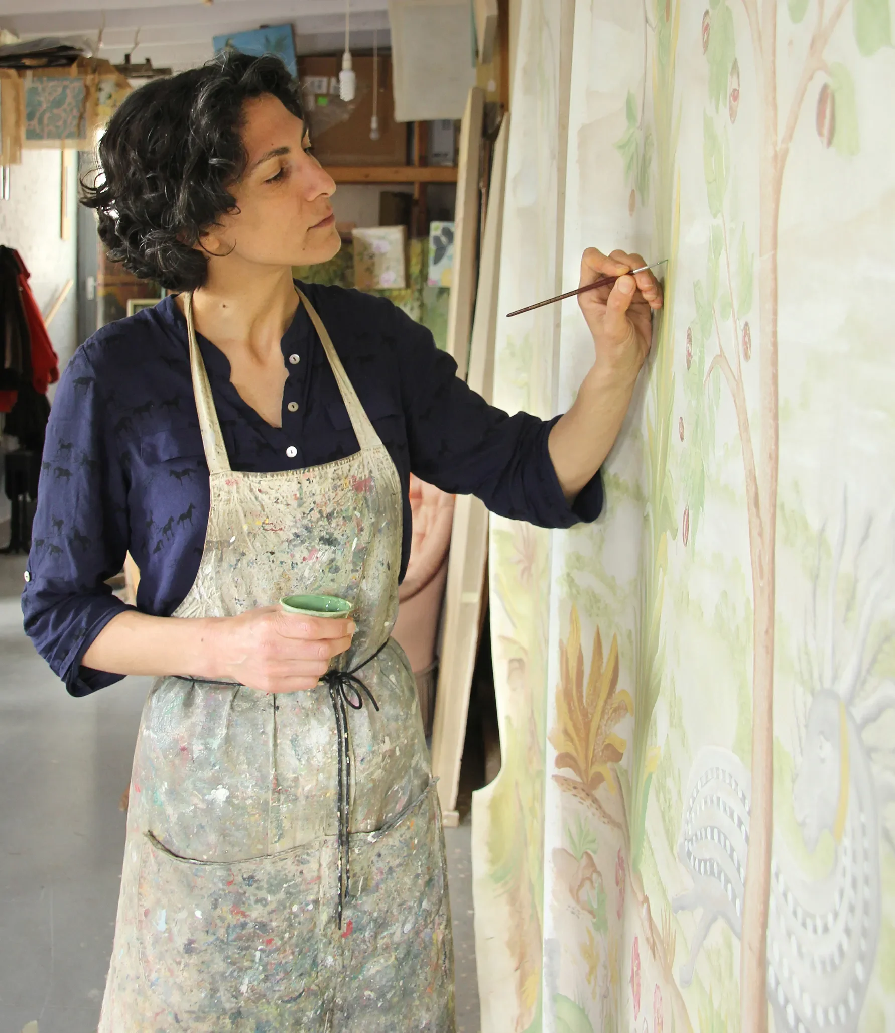 Female artist working on a large colorful painting of a tree on a wall in an art studio.