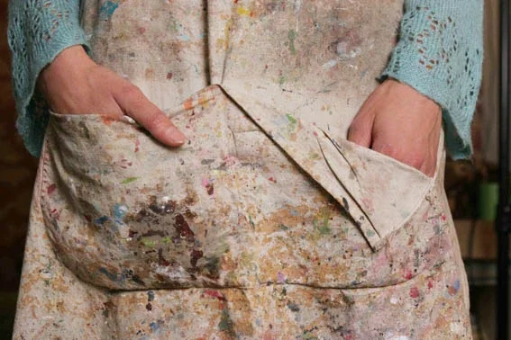 Hands in paint-splattered apron, standing in an artist's studio.