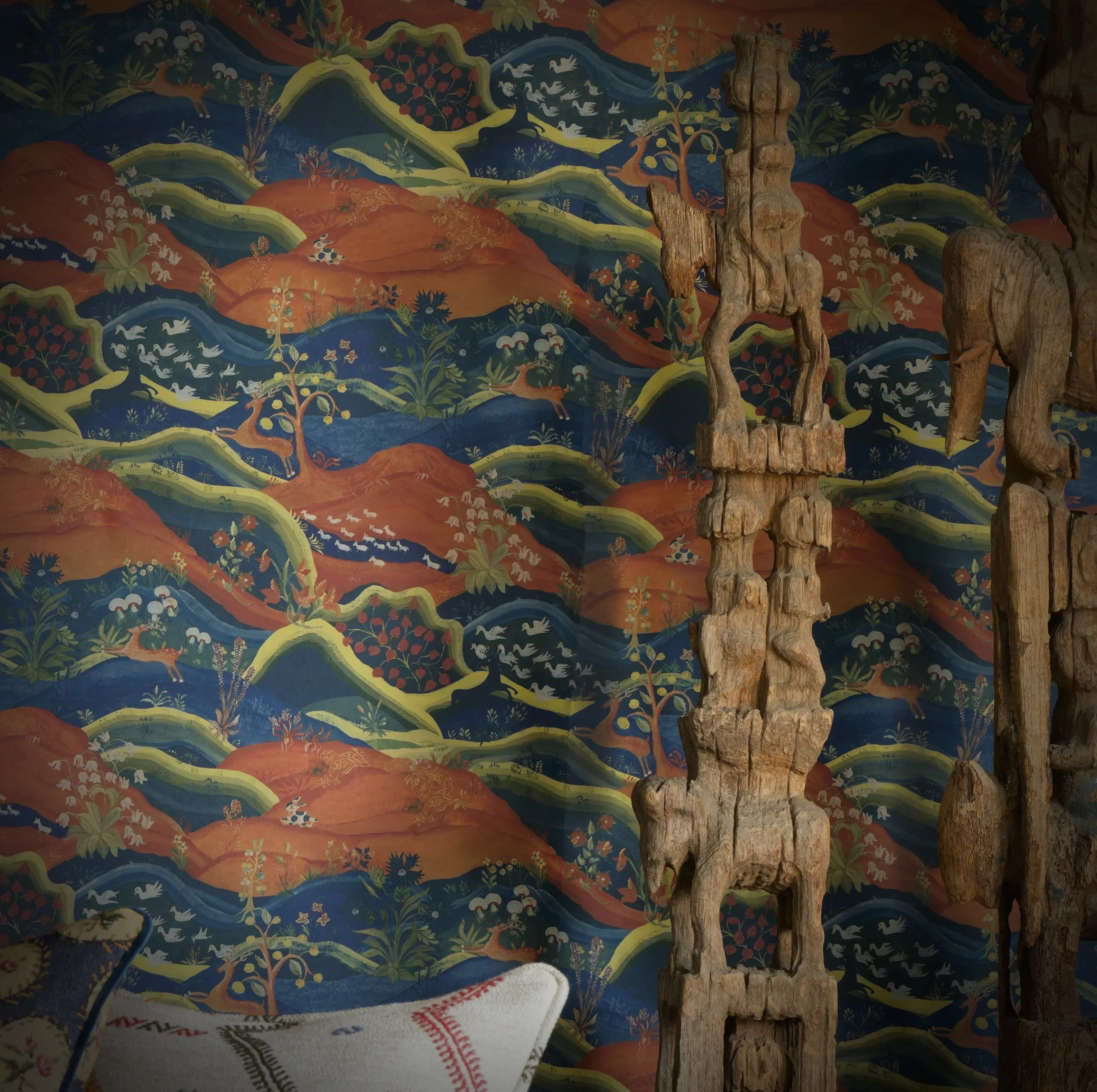 Rufus wallpaper by Melissa White for Andrew Martin in collaboration with Kit Kemp. In the foreground are two ornate wooden carvings.