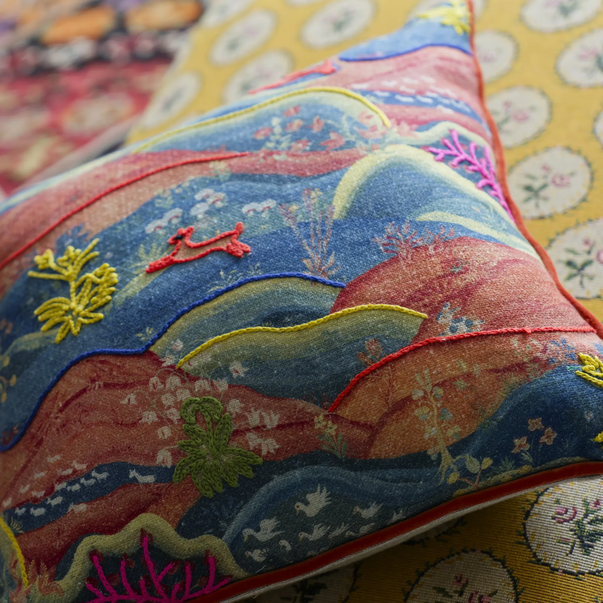 Close-up of a cushion designed by Melissa White for Andrew Martin in collaboration with Kit Kemp. The Meadow Multi cushion has a scenic design with whimsical wildlife stitched in a contrast thread.