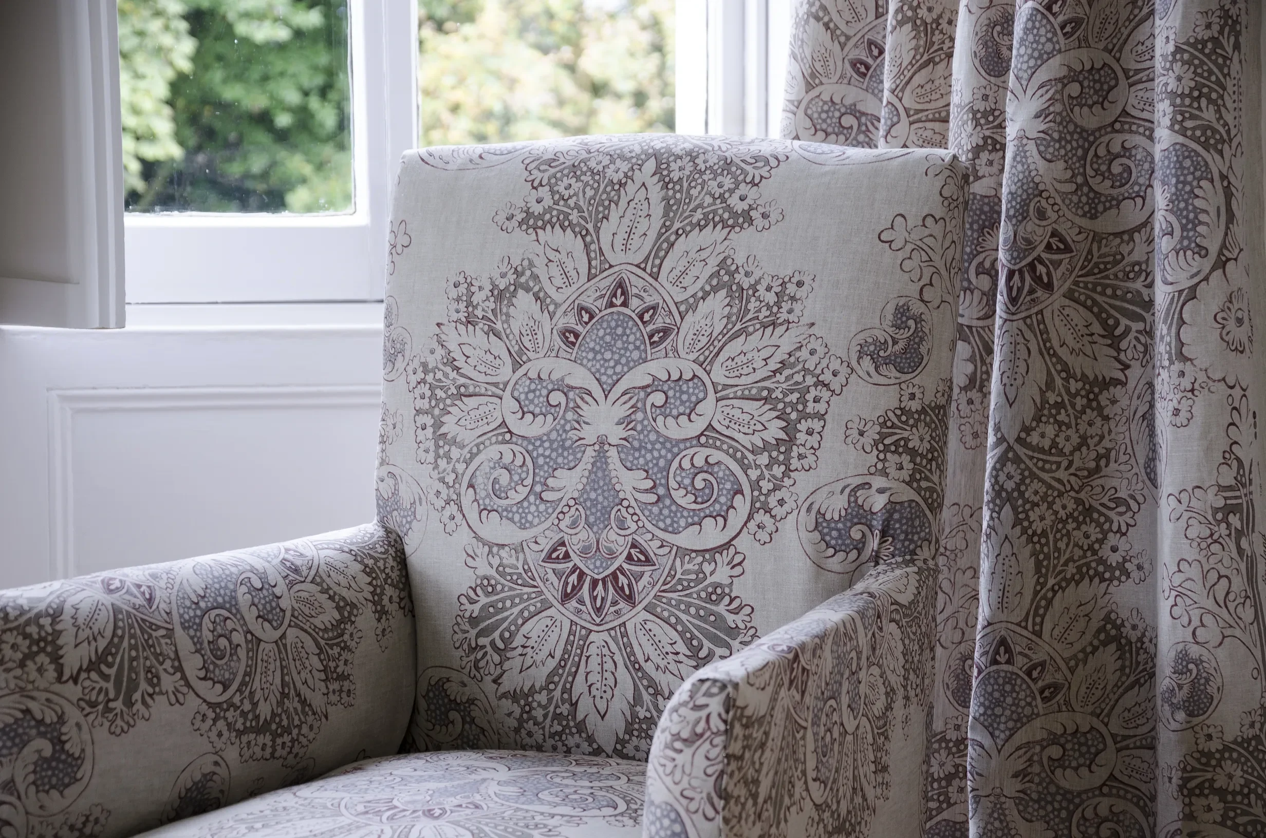 Chair upholstered in Rococo fabric by Melissa White for Lewis & Wood, shown alongside a matching curtain, displaying the hand-painted ornamental repeat design.