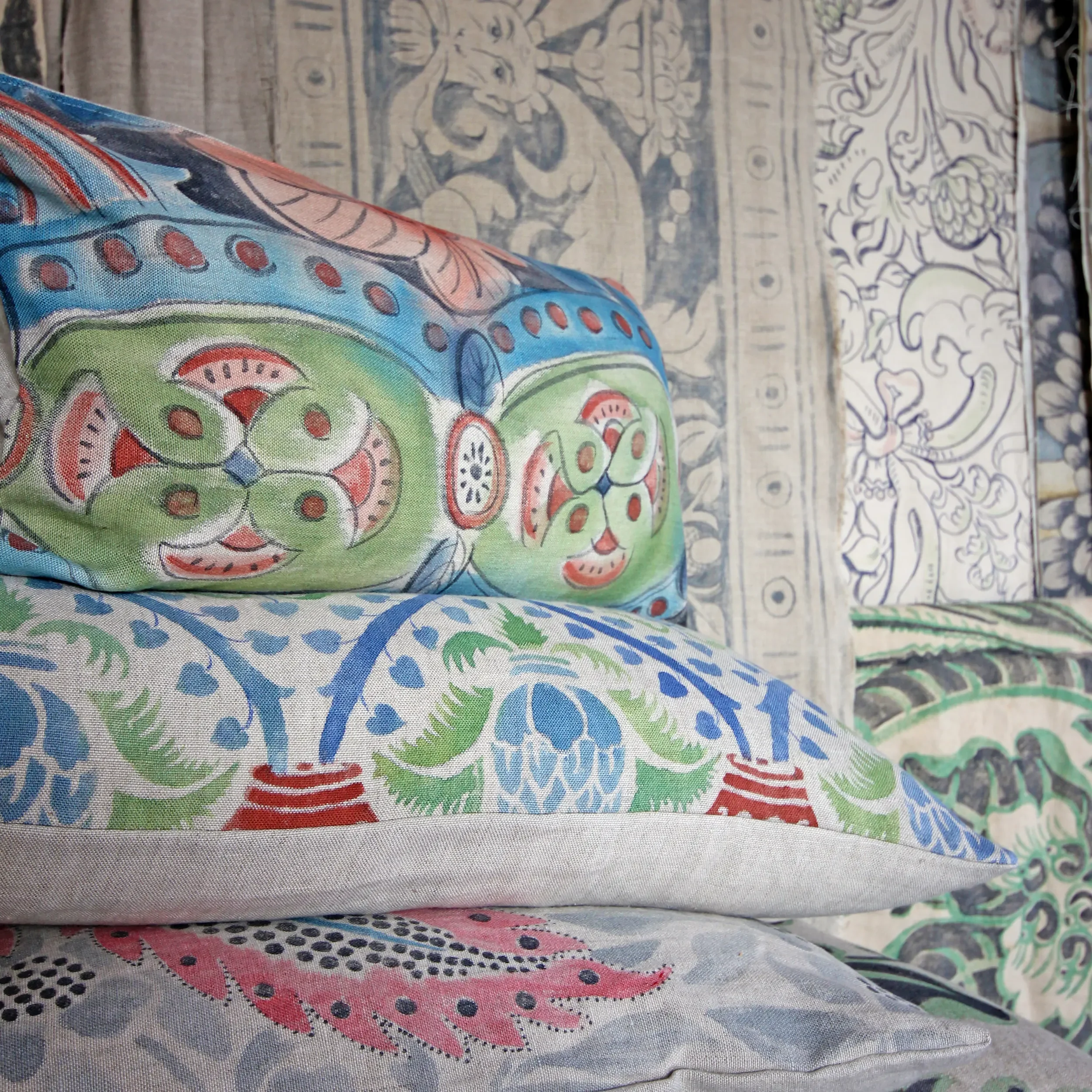 A colorful fabric with patterns of fish and floral motifs draped over other patterned fabrics on a flat surface.