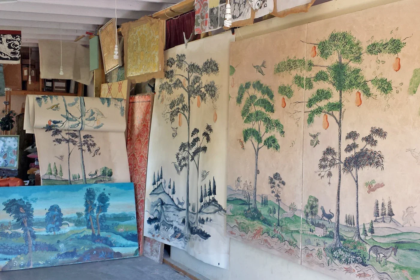A collection of traditional Asian landscape paintings of trees, scenery, and animals hanging on a wall in an art studio.