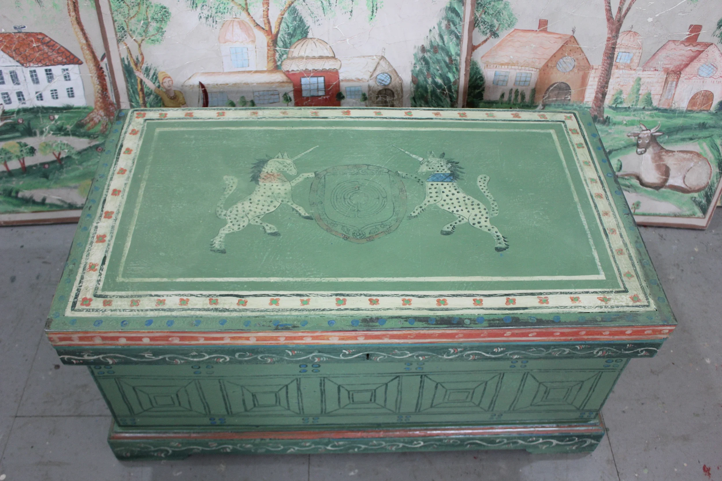 Hand-painted decorative chest by Melissa White, made for Kit Kemp's Drawing Room installation at Bergdorf Goodman, New York, 2019. Green ground with hand-painted unicorns and trompe l'oeil coffering, with Mythical Land mural visible behind.