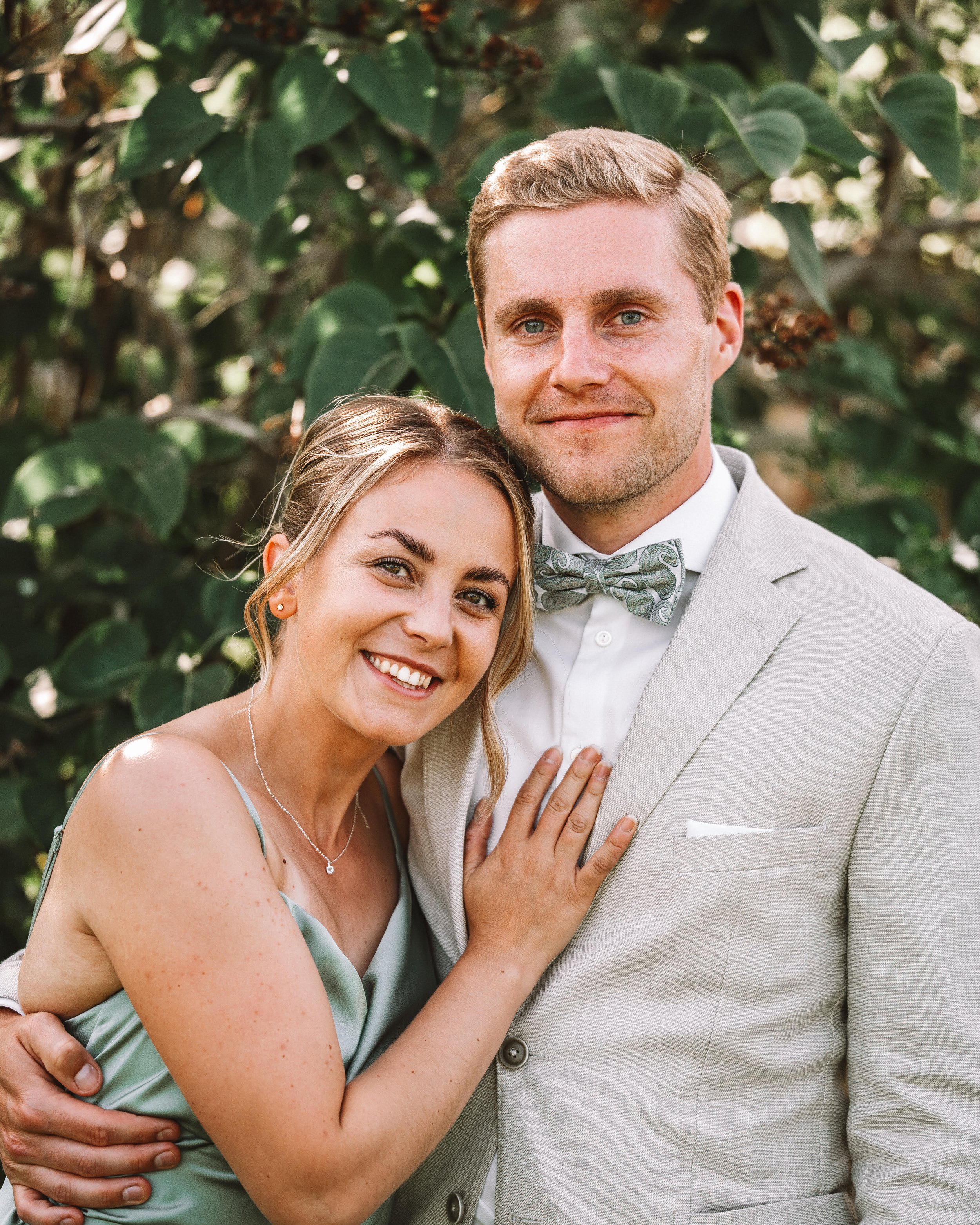 En glad kvinna med ljus hår och en glad man med ljusbrunt hår, står tillsammans utomhus i Örnsköldsvik, Höga Kusten, bland gröna blad, båda ler och ser mot kameran.