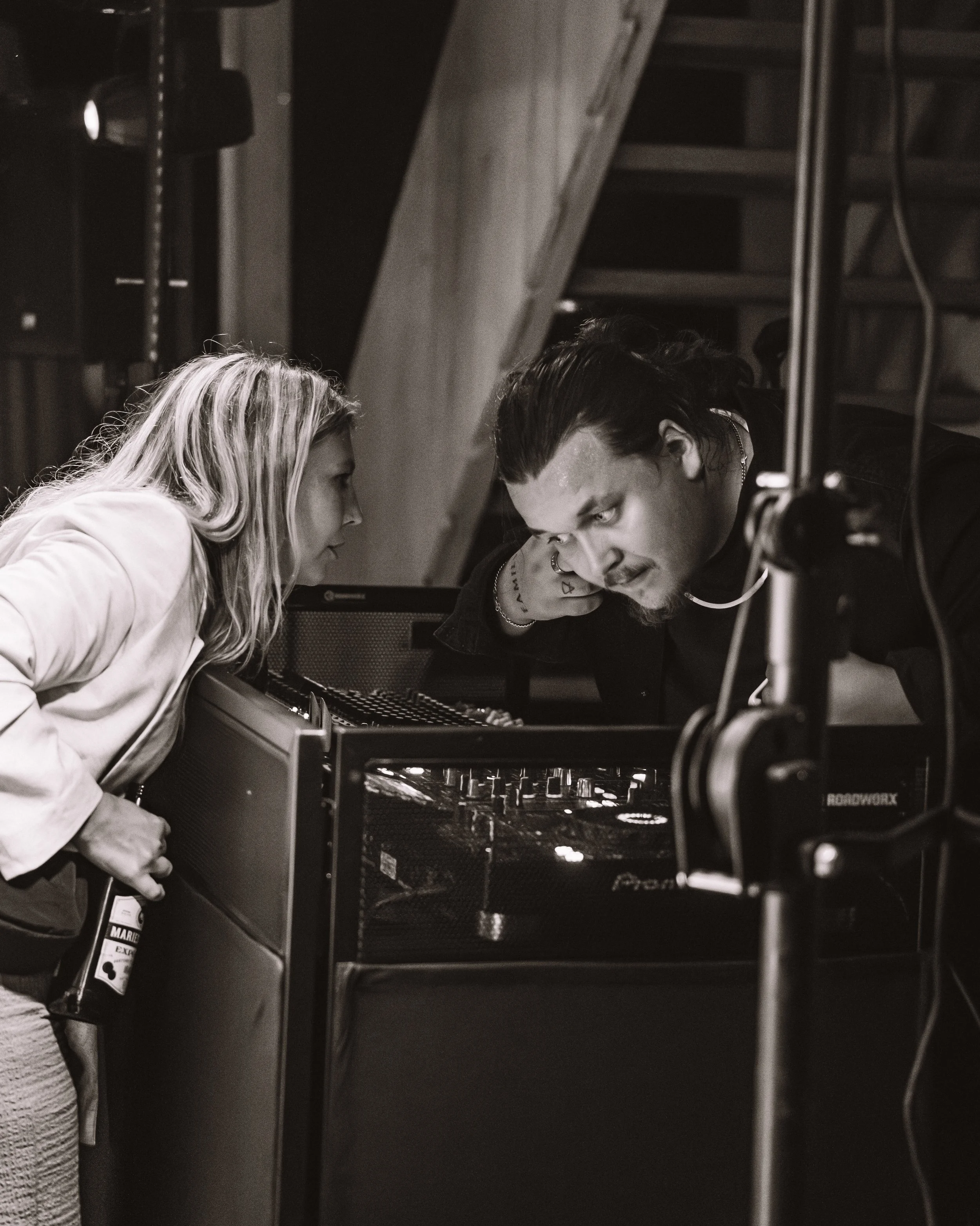 Två personer granskar en DJ-utrustning i ett musikstudio, båda lutar sig över bordet och tittar på kontrollpanelen.