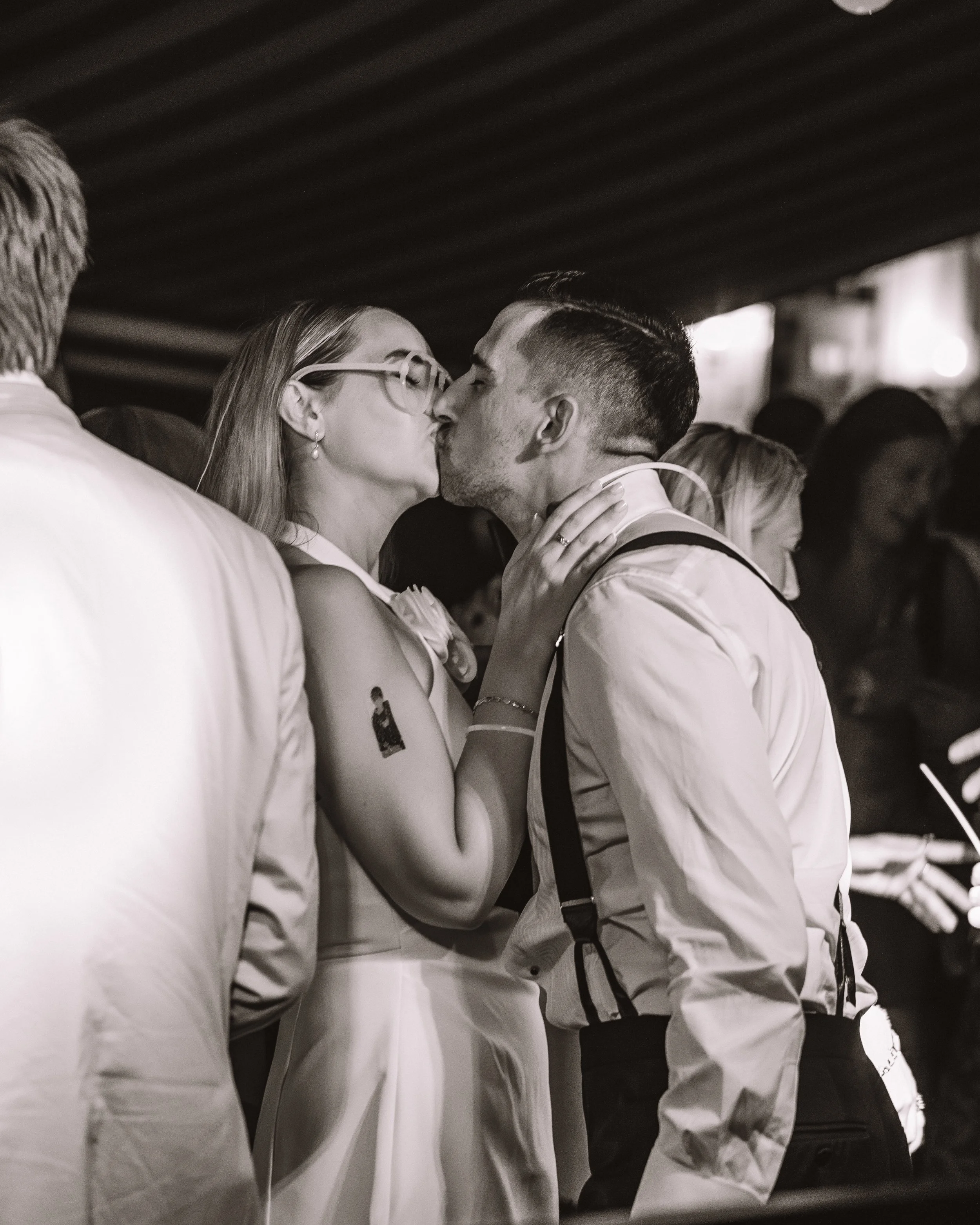 Två personer som kysser i en svartvitbild, omgivna av andra personer.