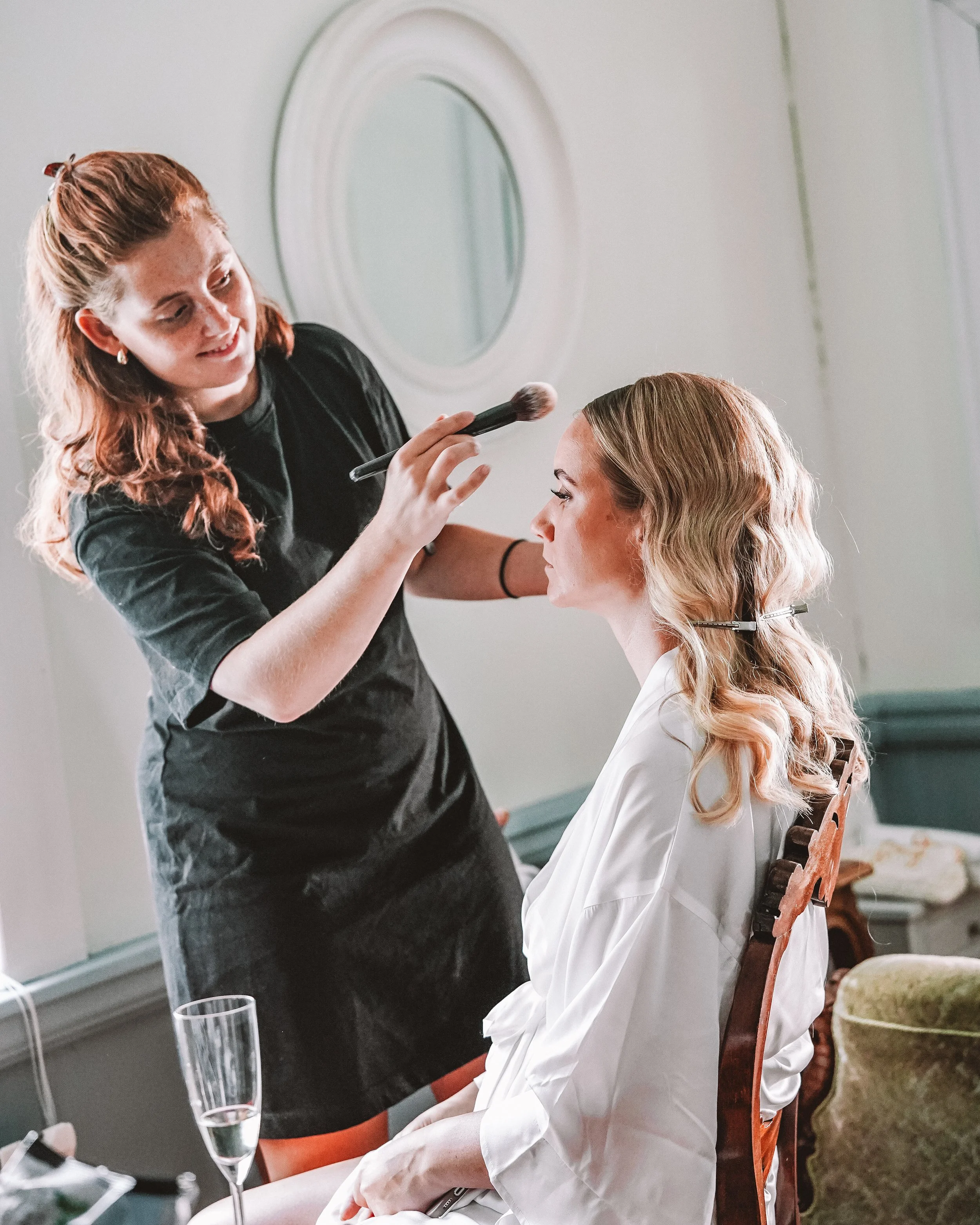 En makeup-artist som applicerar makeup på en kvinna som sitter i en fåtölj.