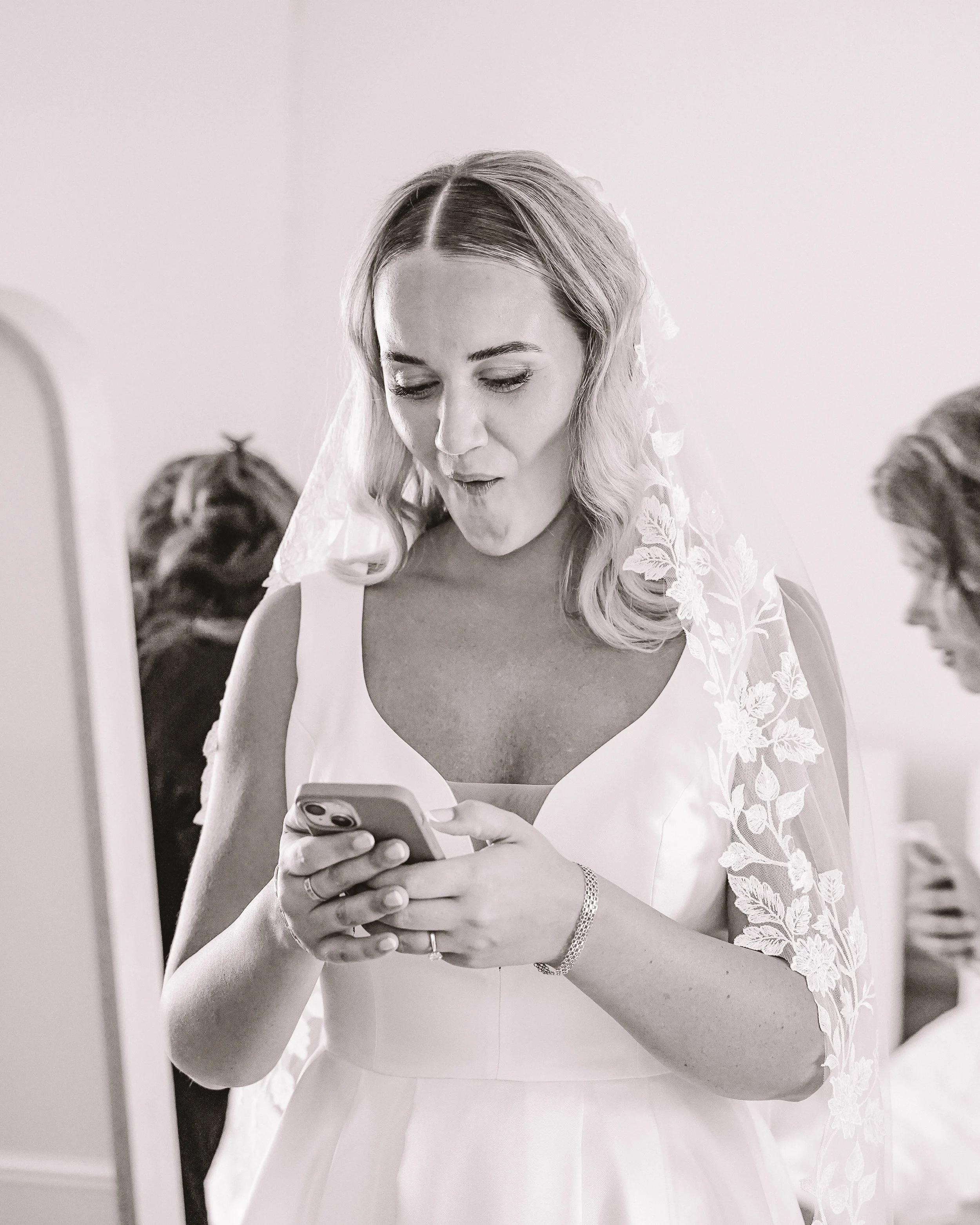 Brud kvinna i vitt brudklänning med slöja, tittar på sin telefon.