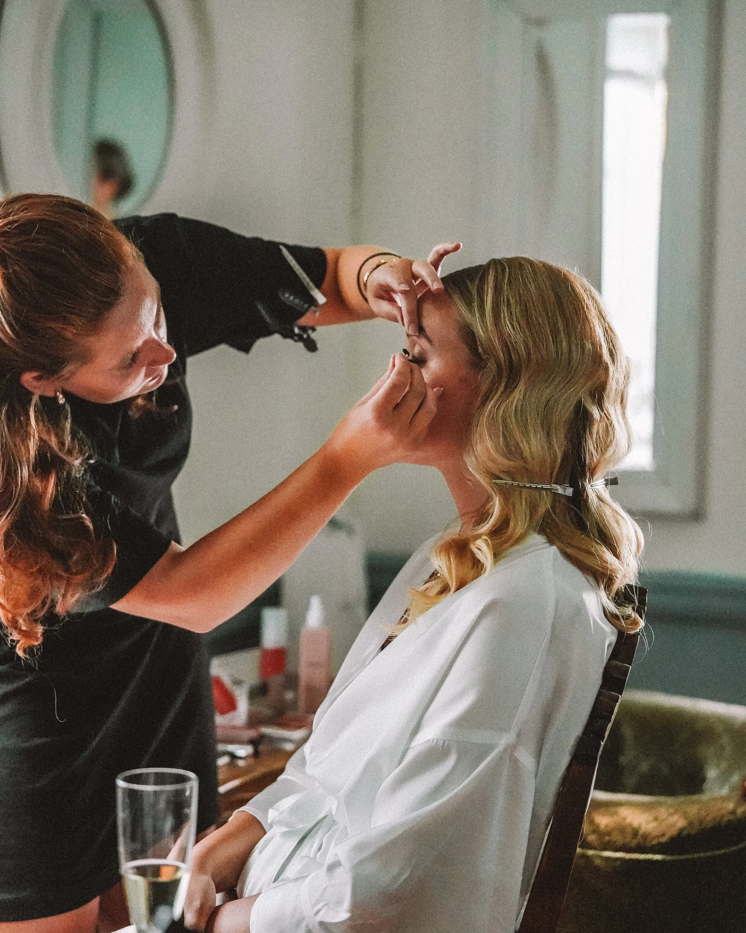 En makeup-artist som applicerar smink på en kvinna som sitter i en stol i ett rum.