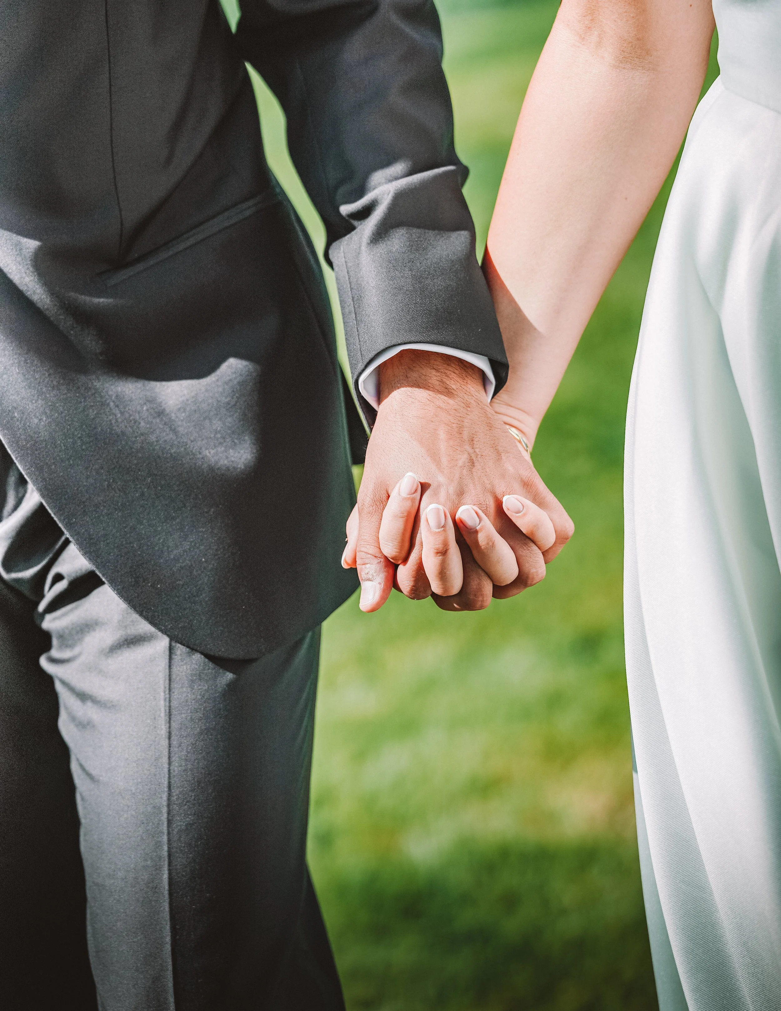 Två personer håller händer i en utomhusmiljö, troligen på bröllop.