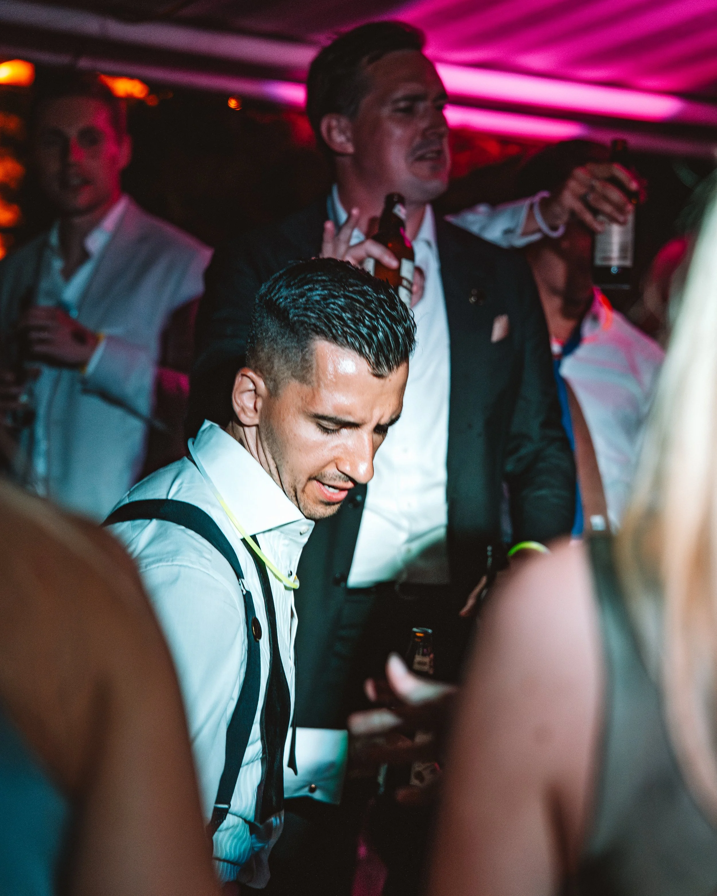 Flera personer dansar och dricker på en fest eller nattklubb med rosa och lila belysning.