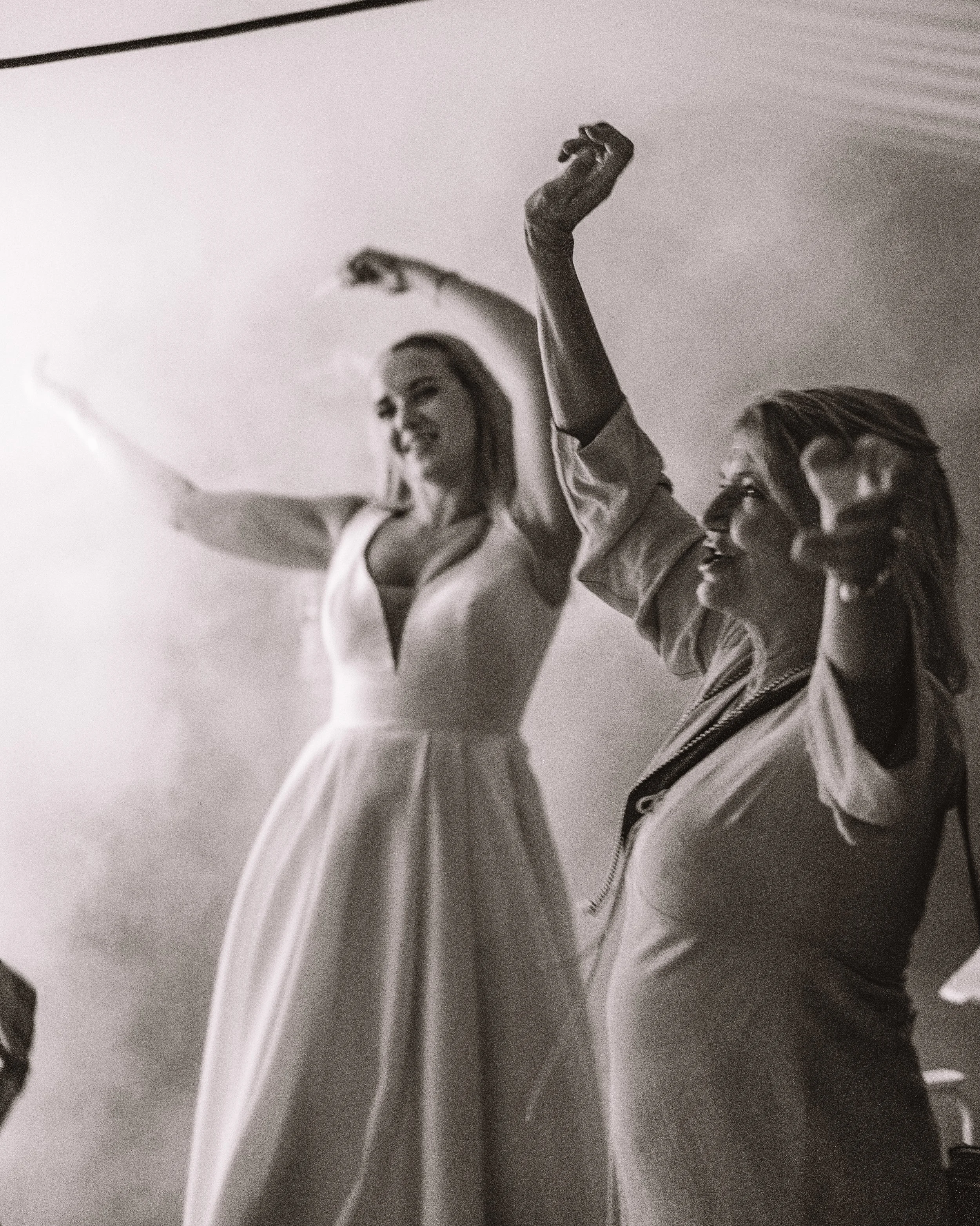 Två kvinnor som dansar och ler, en i en klänning och den andra i en jacka, i en svartvit bild.